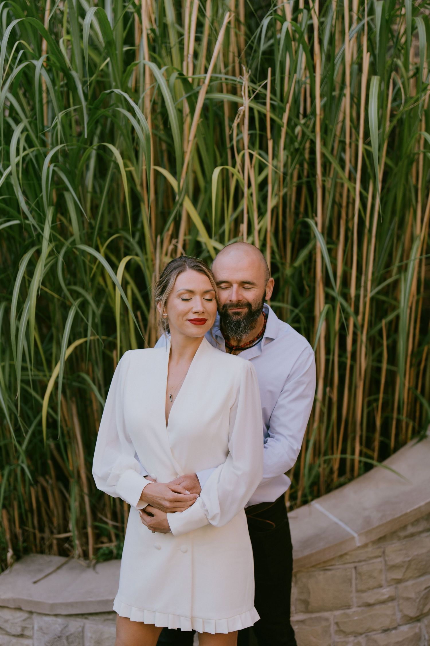 Romantic portrait of couple in front of tall decorative grass wall, embracing naturally