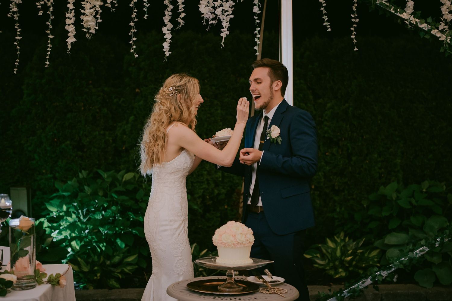 Bride laughing as she playfully smears cake on groom’s face during reception