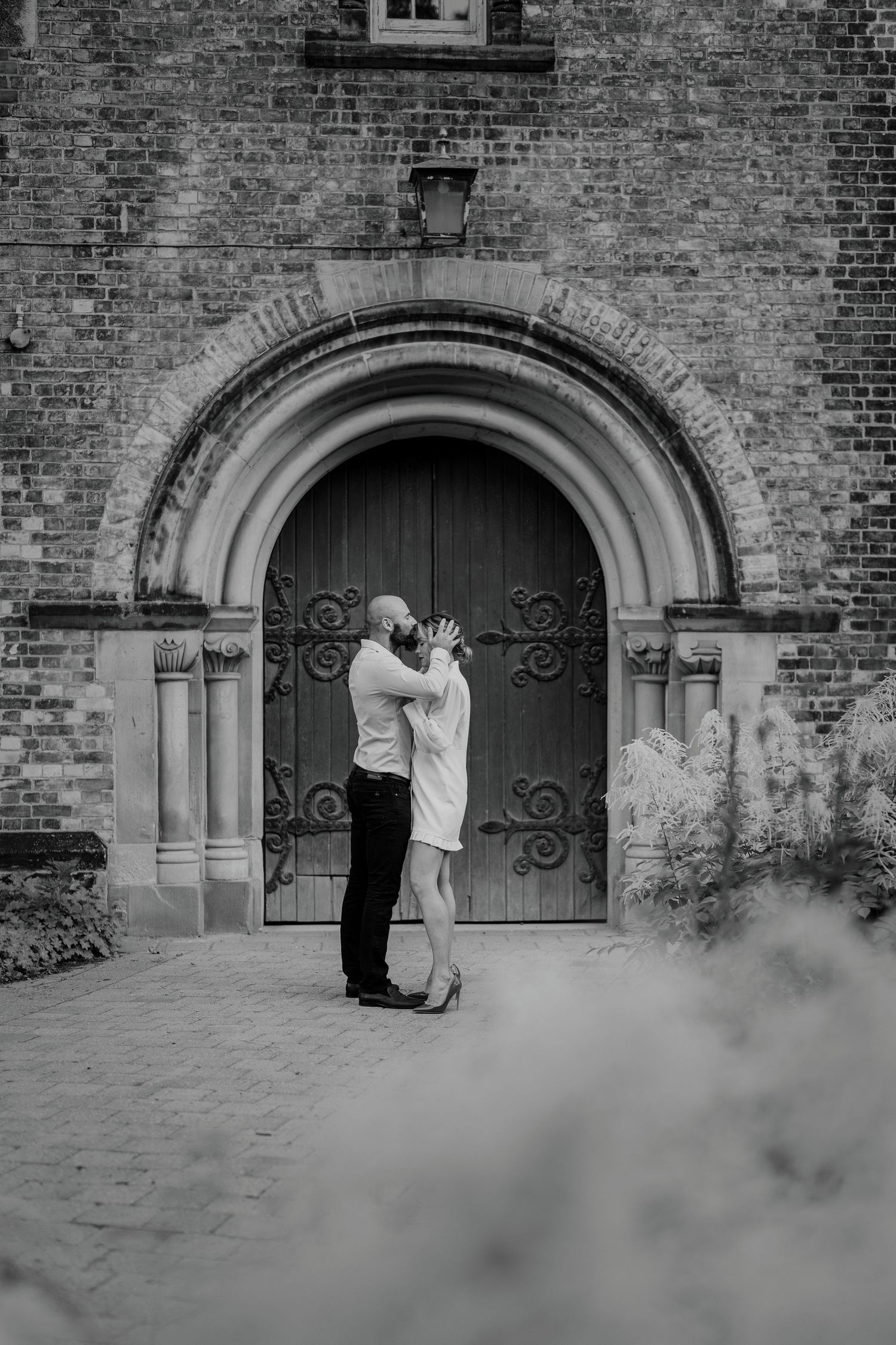 Black and white photo of couple kissing in front of romantic arched wooden door
