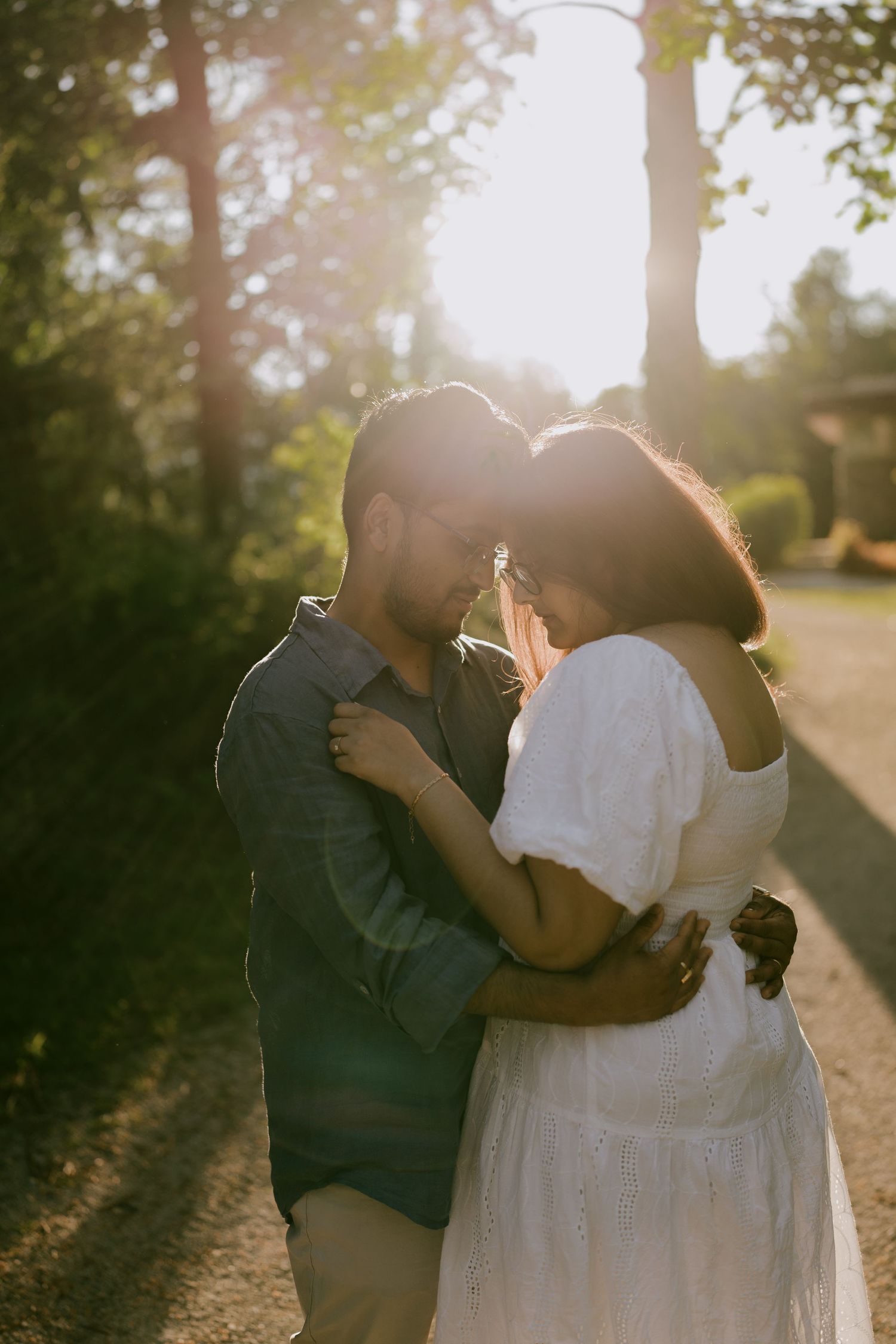 Golden hour engagement photo of couple hugging on tree-lined path with sun flare