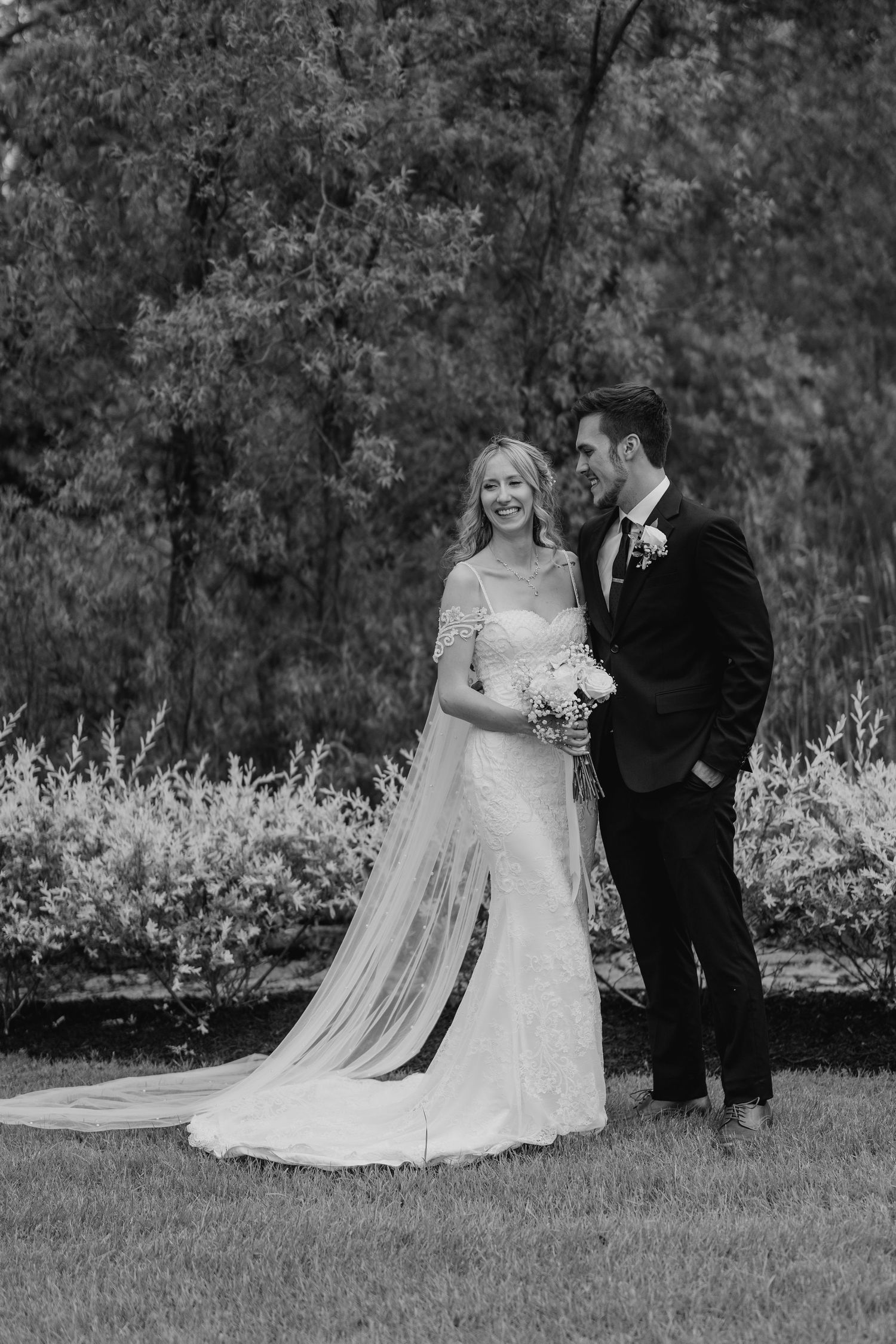 Black and white portrait of bride and groom standing in garden