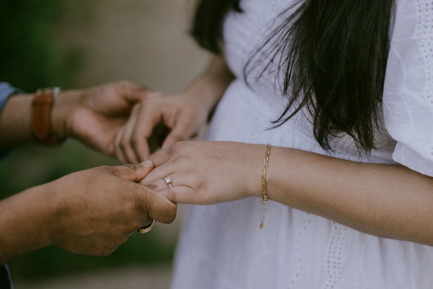 Close-up photo of groom placing engagement ring on partner’s hand
