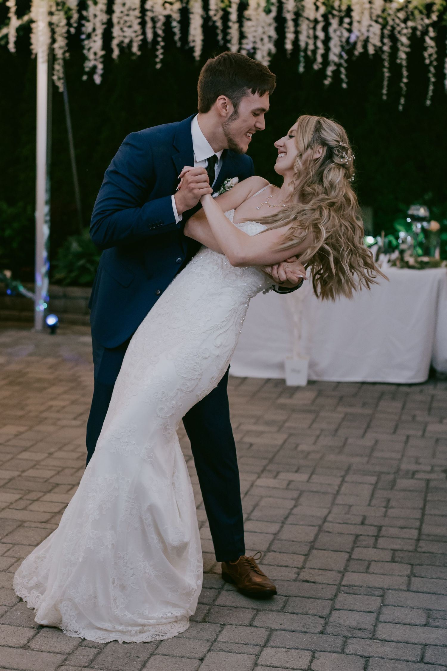 Groom dipping bride during wedding dance under evening lights