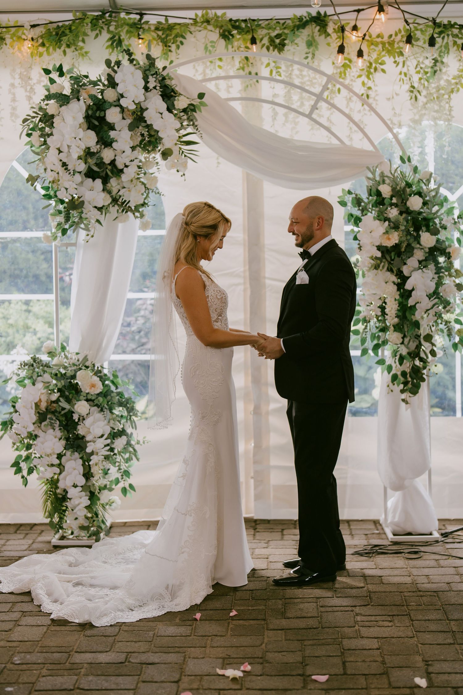 Bride and groom exchanging vows under floral arch during indoor wedding ceremony in Oshawa, Ontario