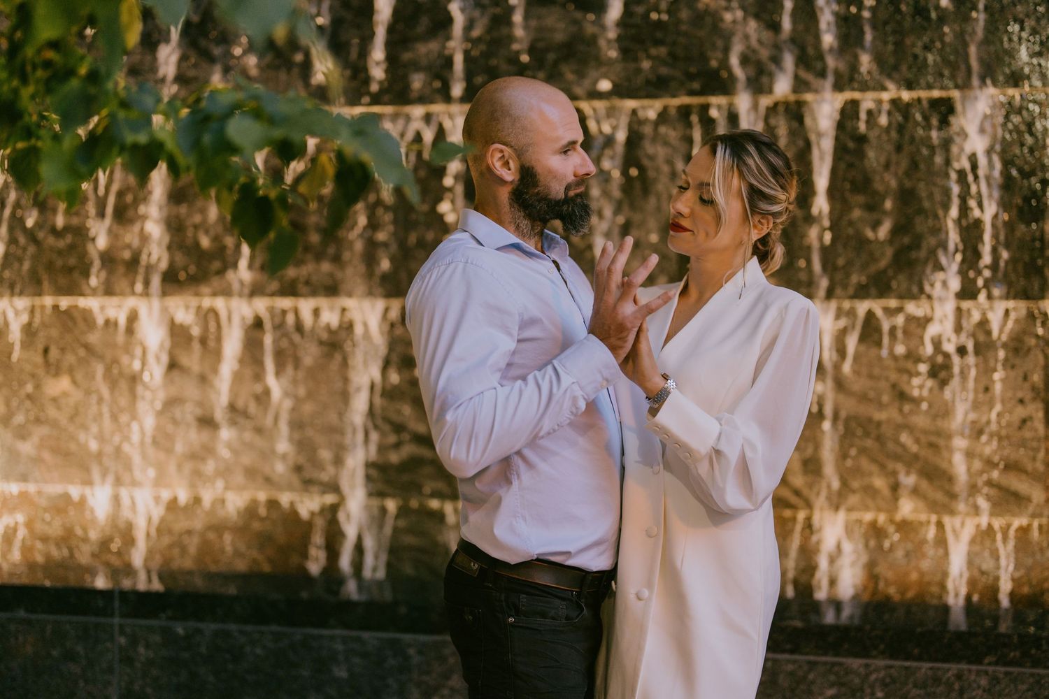 Candid couple photo with natural smiles in front of textured stone wall