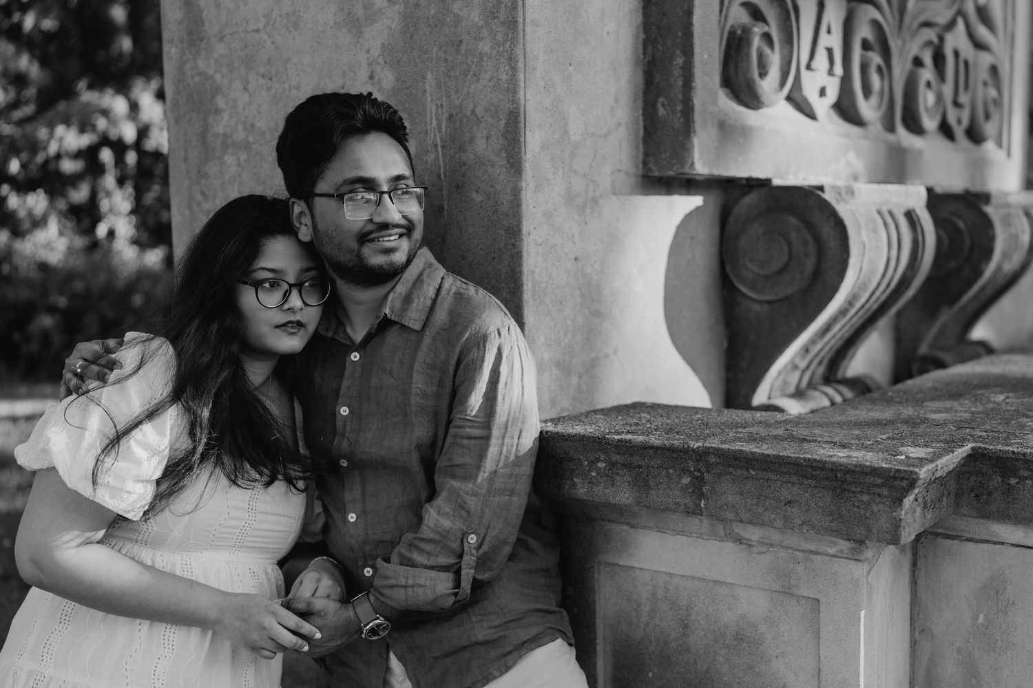Black and white photo of couple cuddling beside carved stone railing