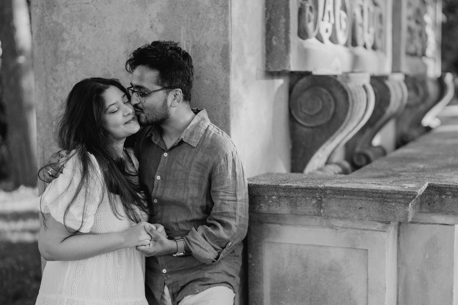 Black and white photo of couple embracing beside carved stone railing
