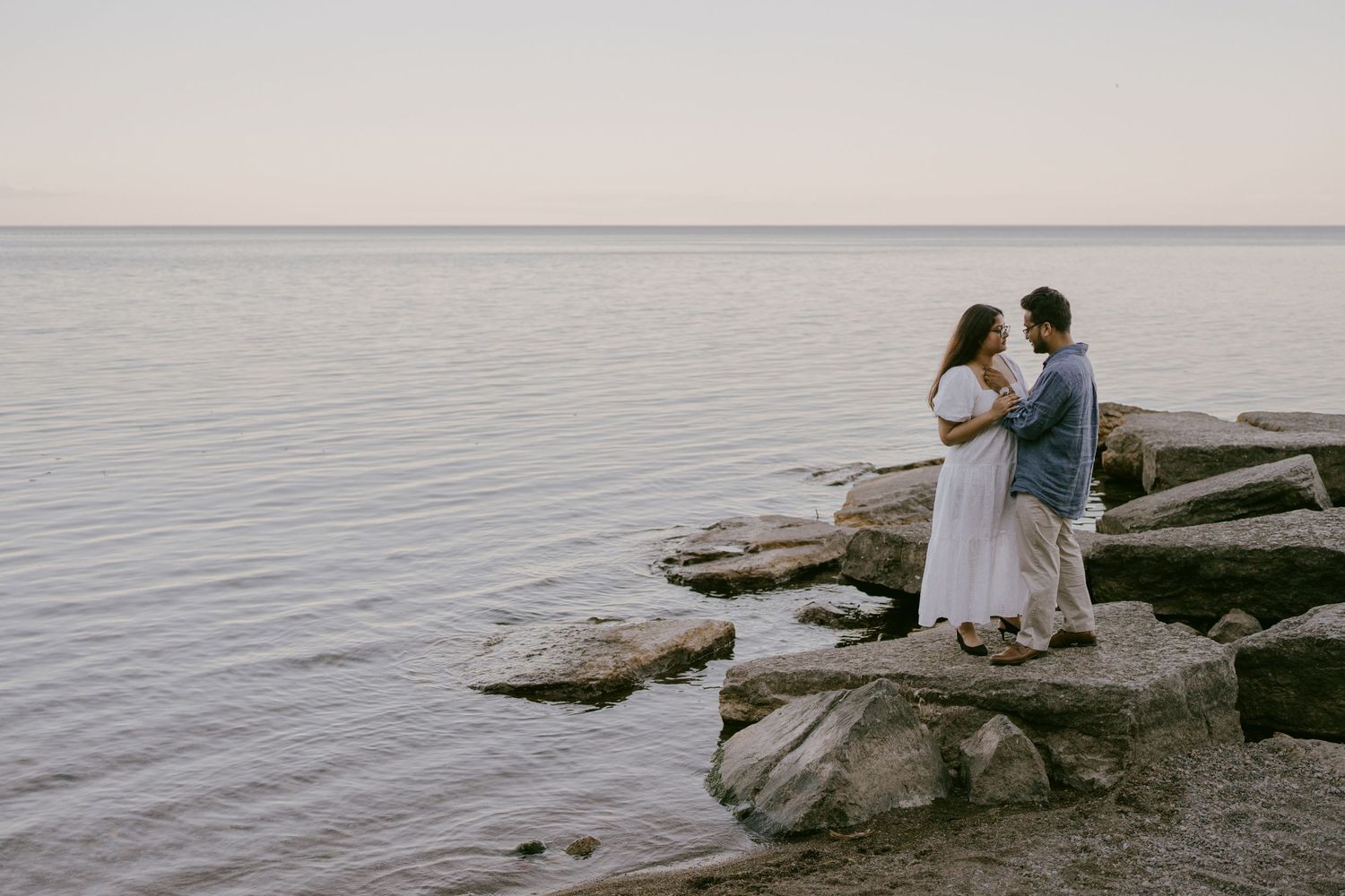 Engagement photo of couple standing on shoreline rocks at dusk