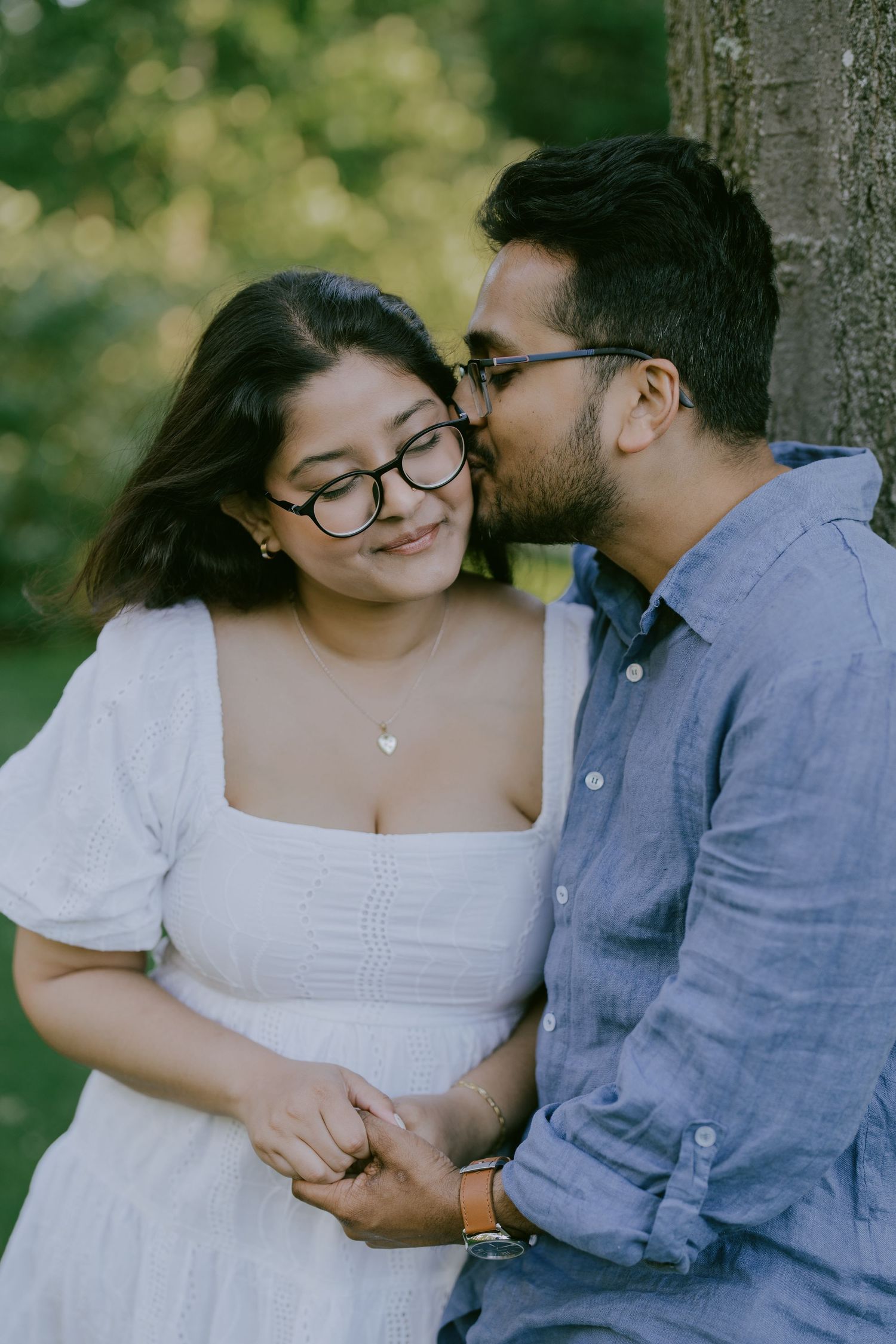 Color photo of couple smiling while holding hands near a tree