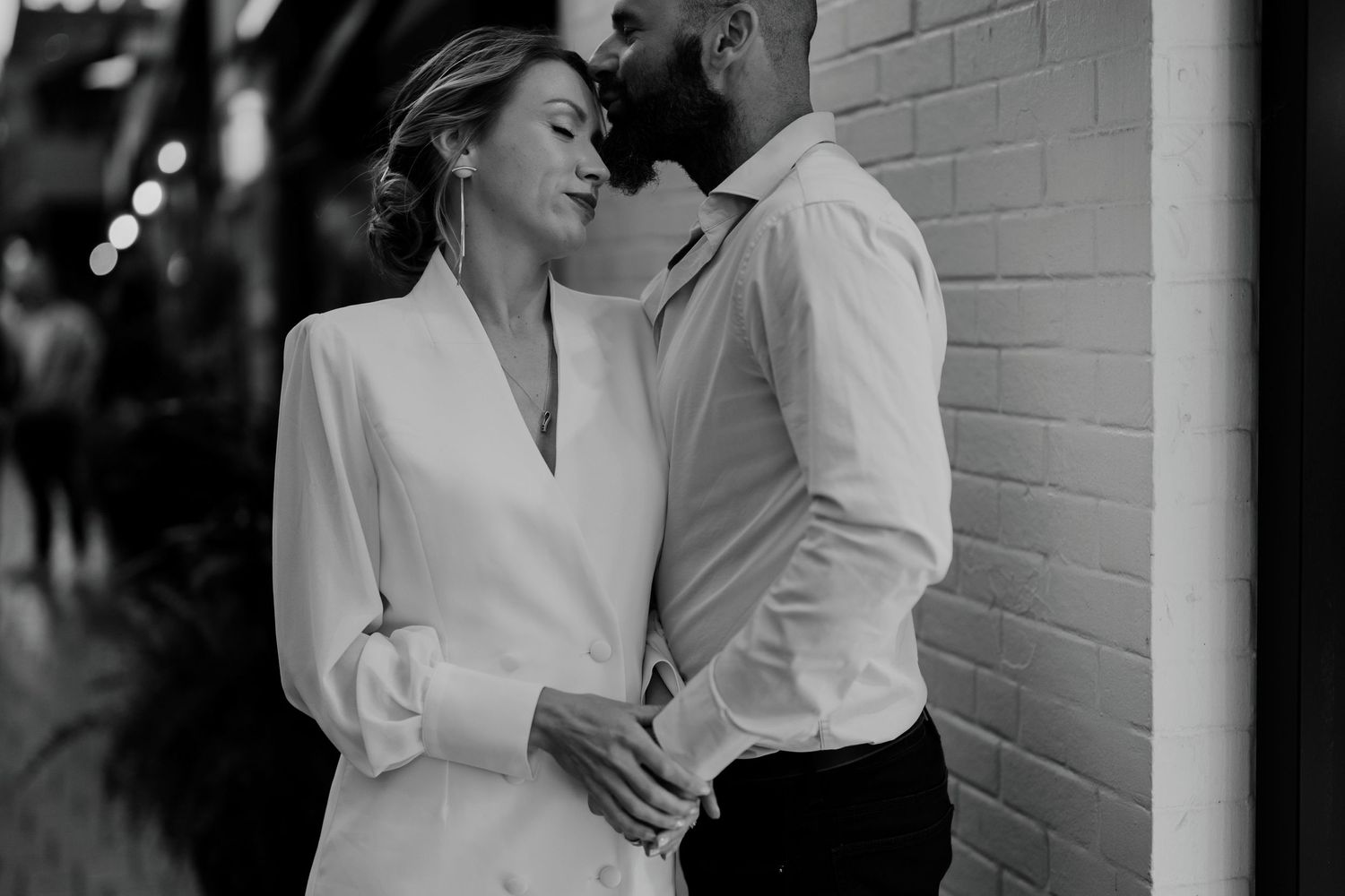 Romantic black and white photo of couple standing close near a city brick wall at night