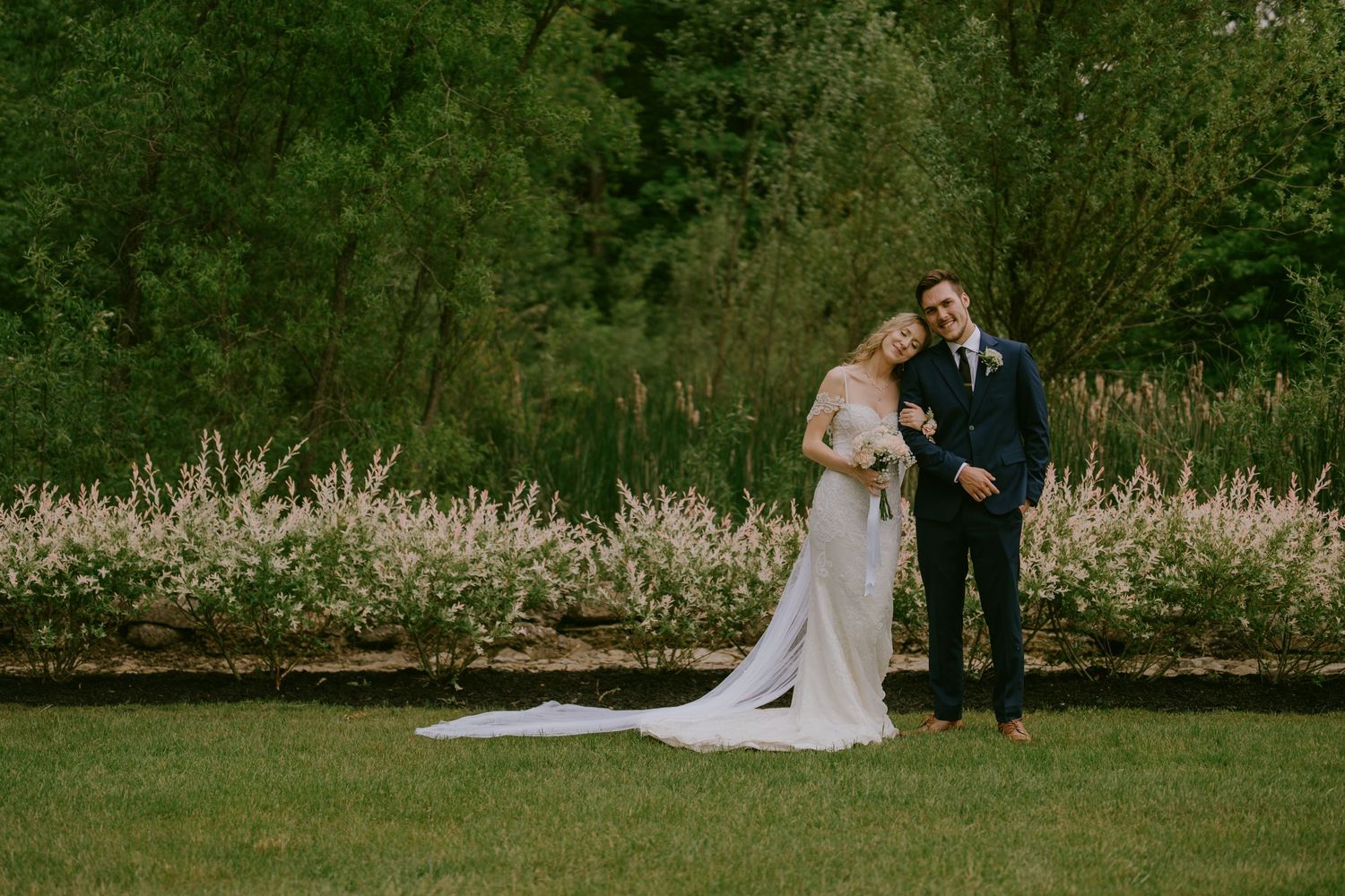 Bride resting head on groom’s shoulder in lush garden setting