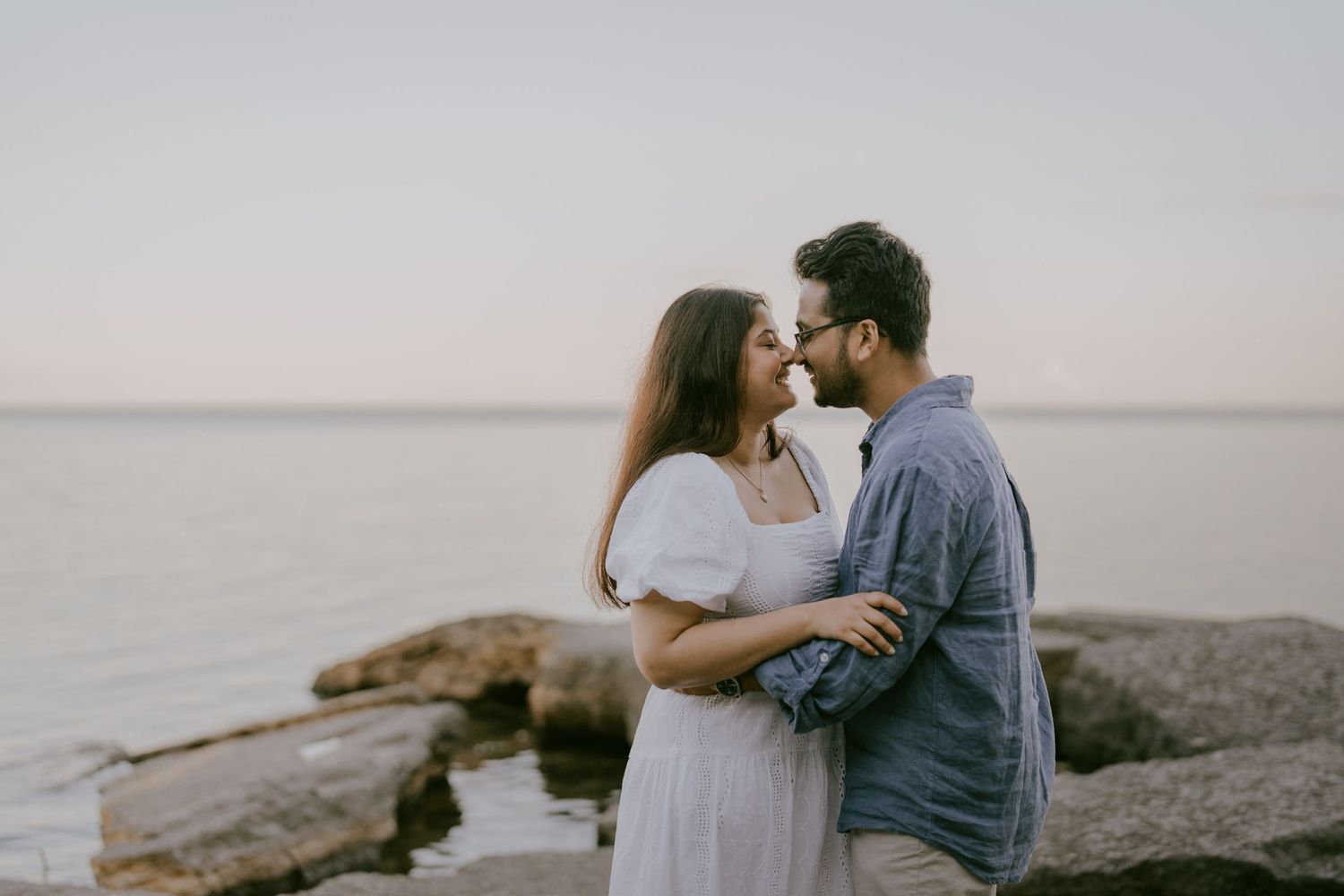 Soft and romantic engagement photo of couple gazing at each other near lake rocks