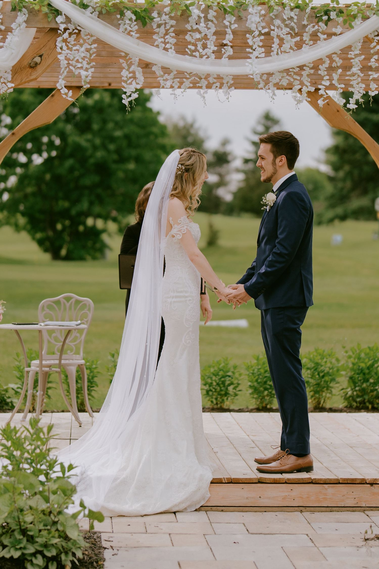 Bride and groom holding hands under floral arch while exchanging vows