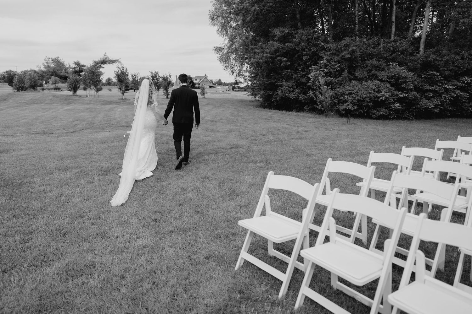 Black and white image of couple walking past ceremony seating on lawn