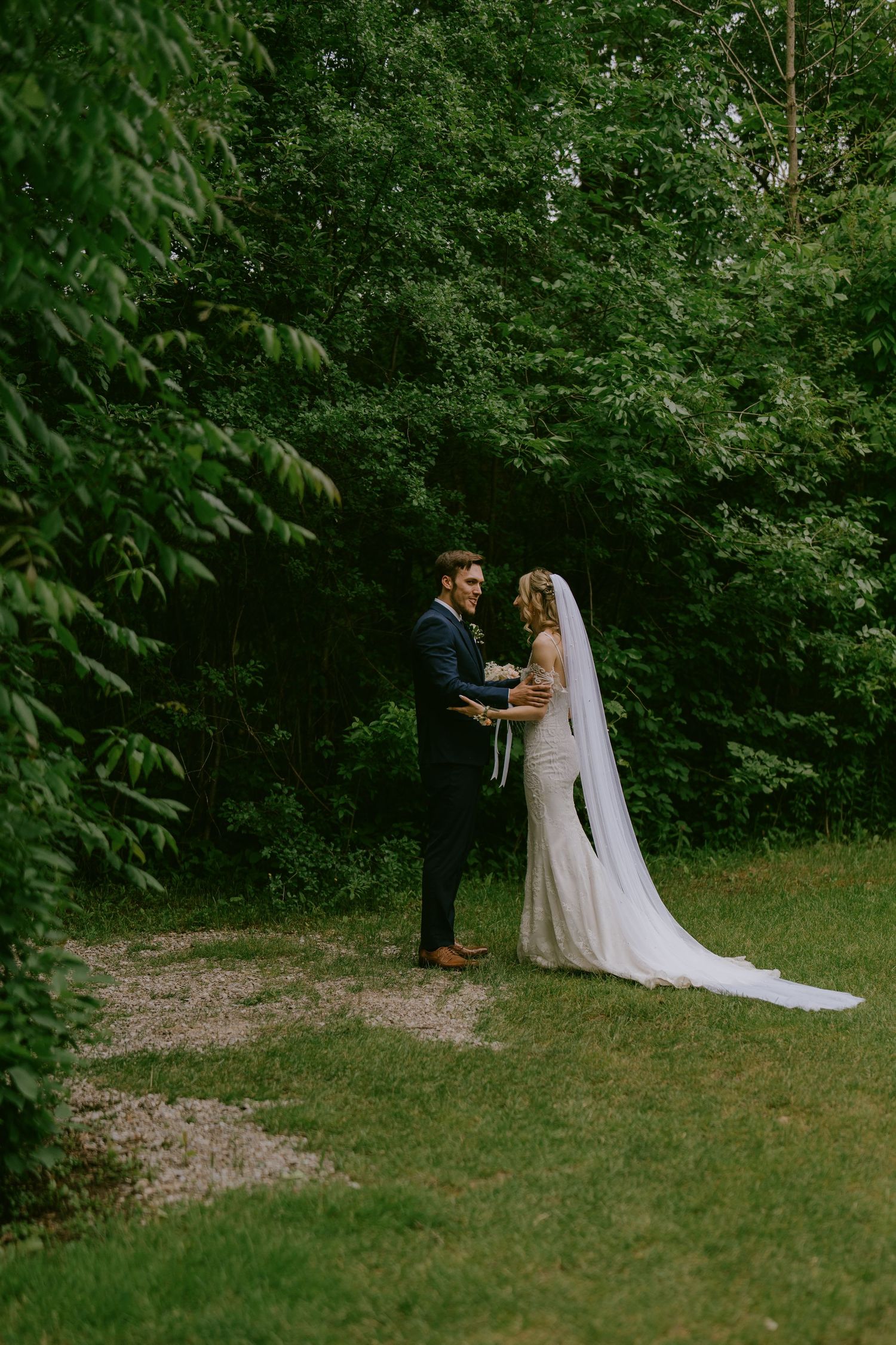 Bride and groom standing in wooded garden path holding hands