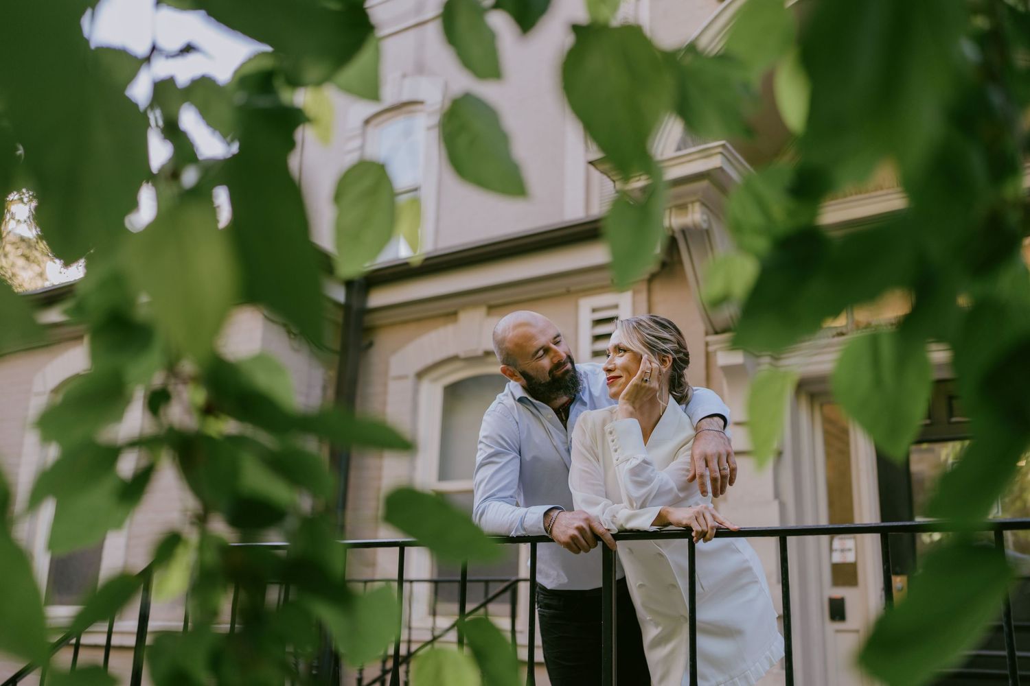 Romantic couple portrait on outdoor balcony, framed by green leaves
