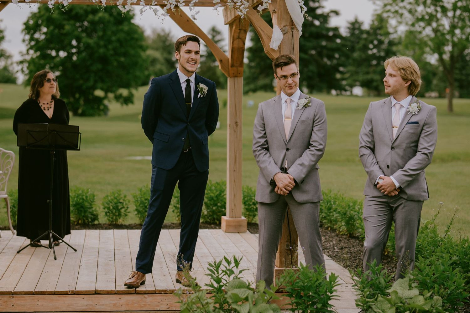 Groom smiling as he watches his bride walk down the aisle at outdoor ceremony
