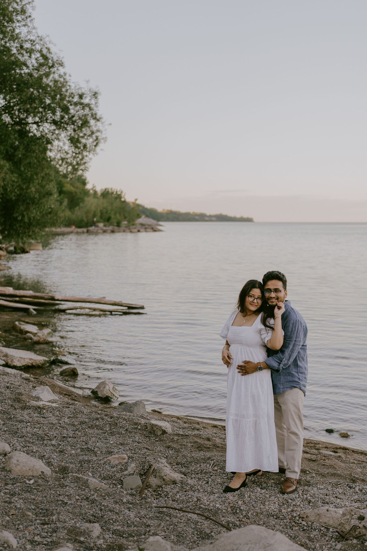 Golden hour engagement photo of couple embracing by the water’s edge
