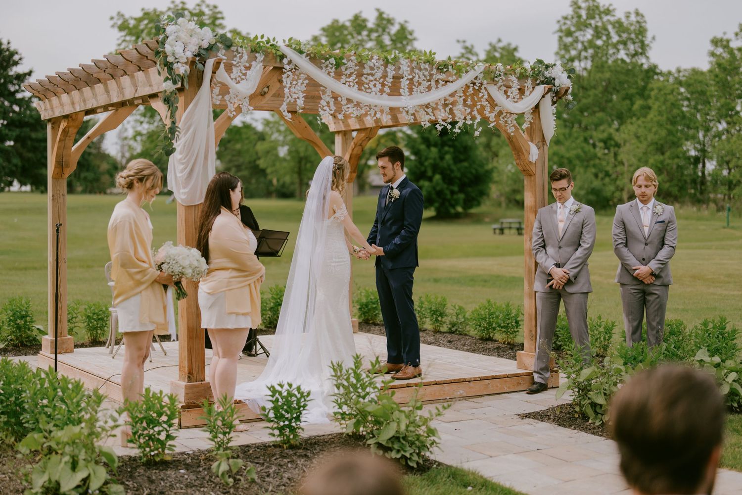 Bride and groom exchanging vows under wooden arch during ceremony
