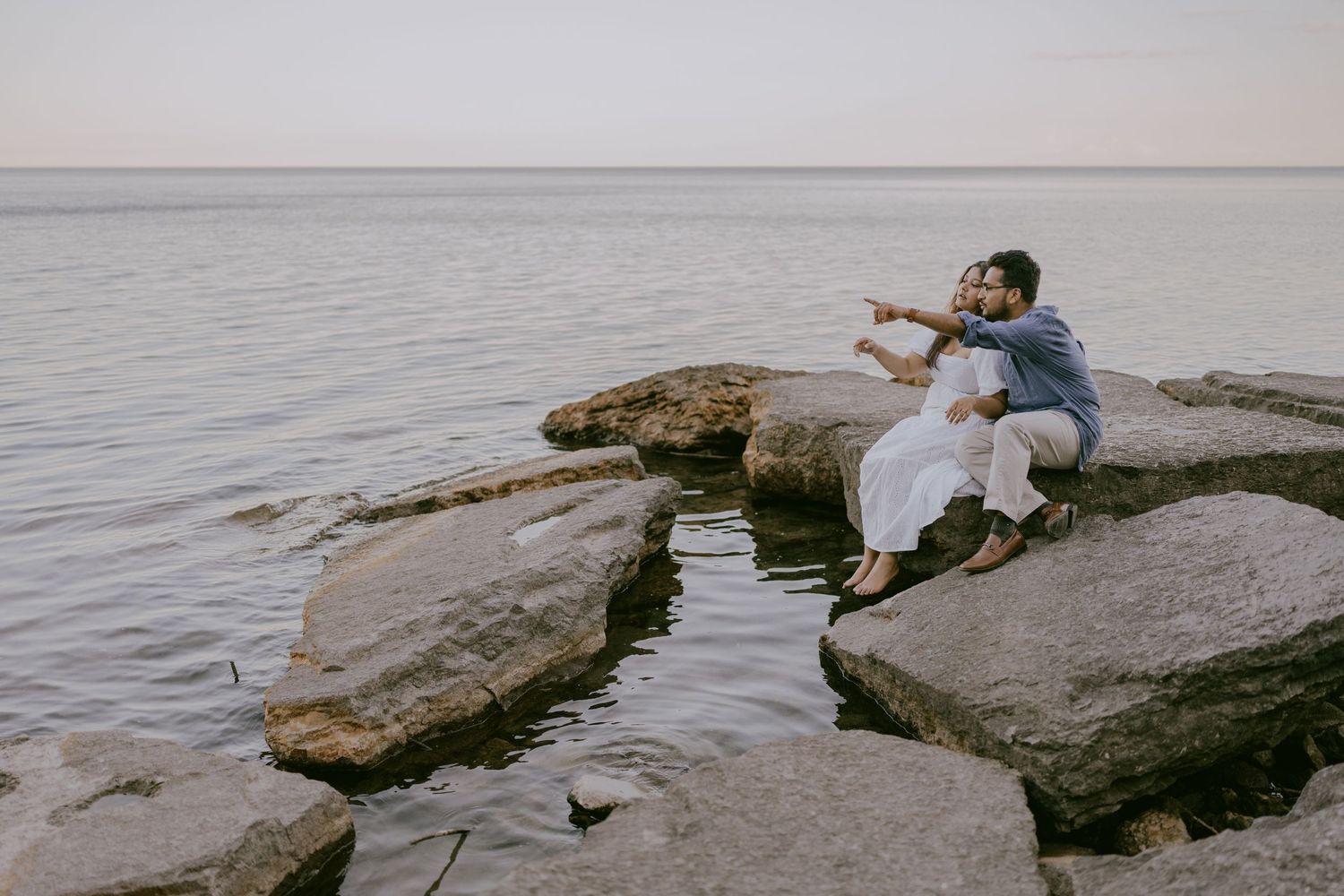 Couple sitting together on lakefront rocks during golden hour