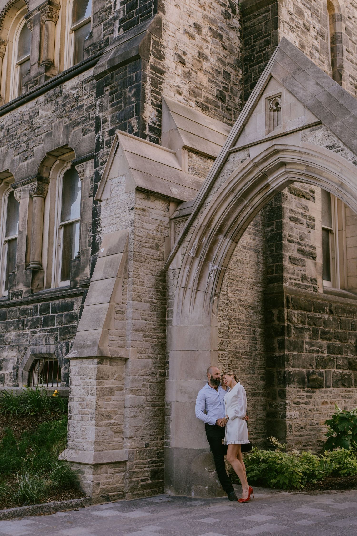 Romantic photo of couple standing beneath a grand historic stone arch