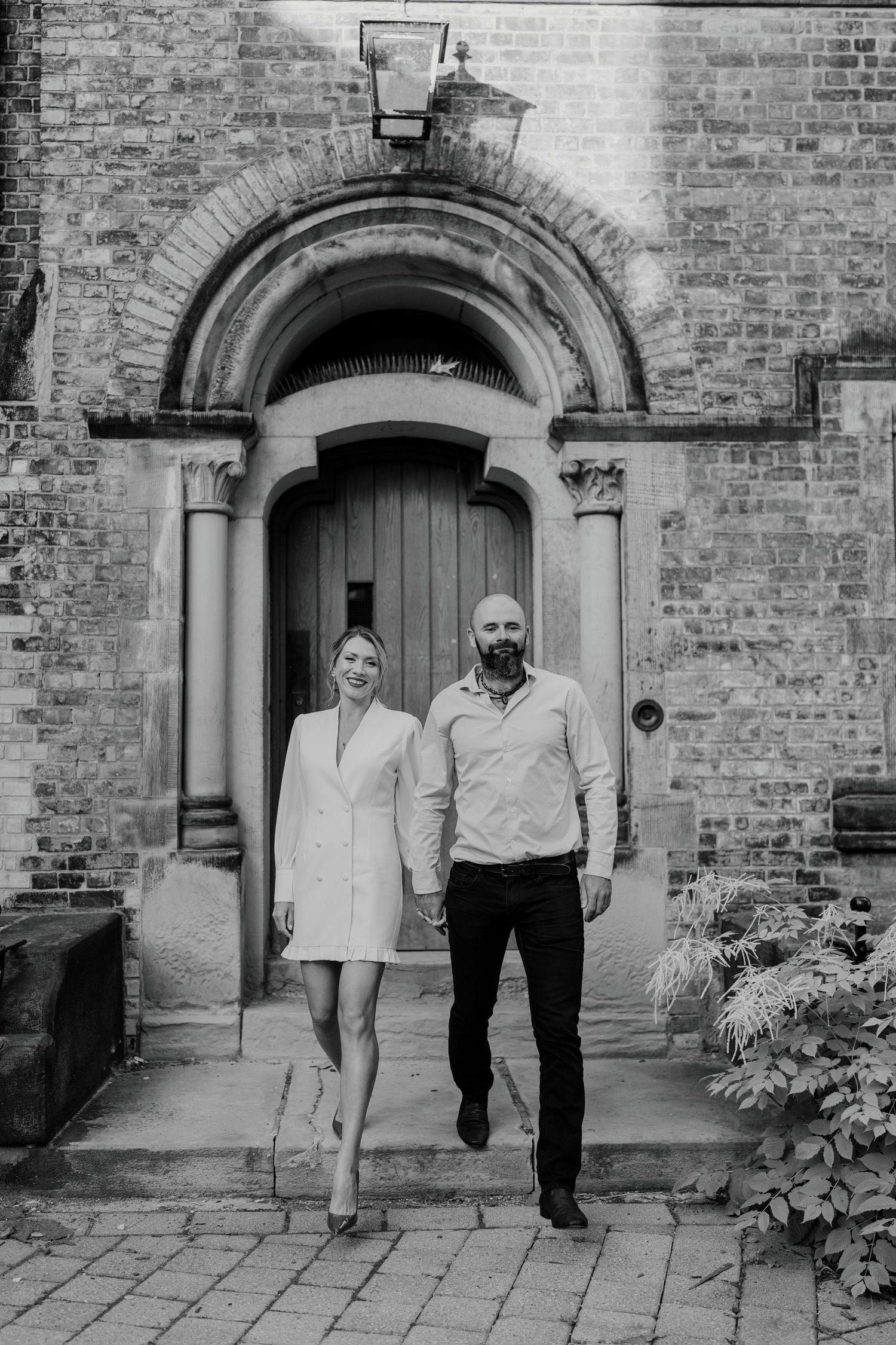 Timeless black and white engagement photo of couple walking past a historic arched doorway