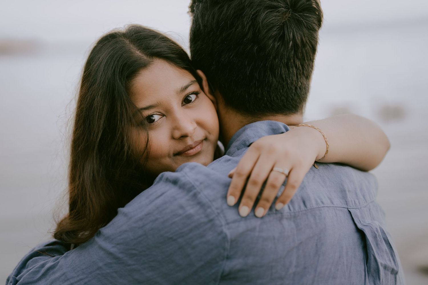 Engagement photo of woman smiling while embracing partner near lake