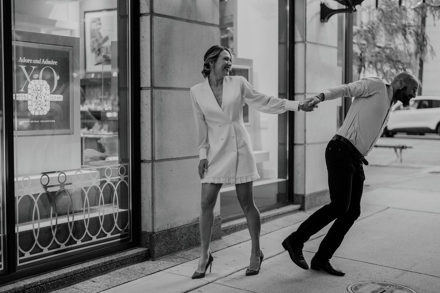 Playful black and white street portrait of couple laughing and pulling each other forward