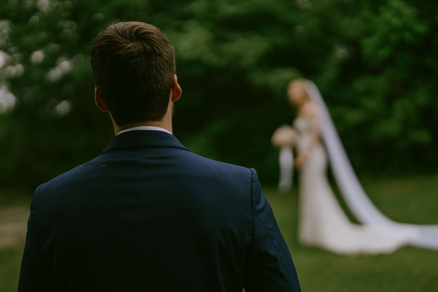 Groom’s perspective of bride standing in field with veil flowing