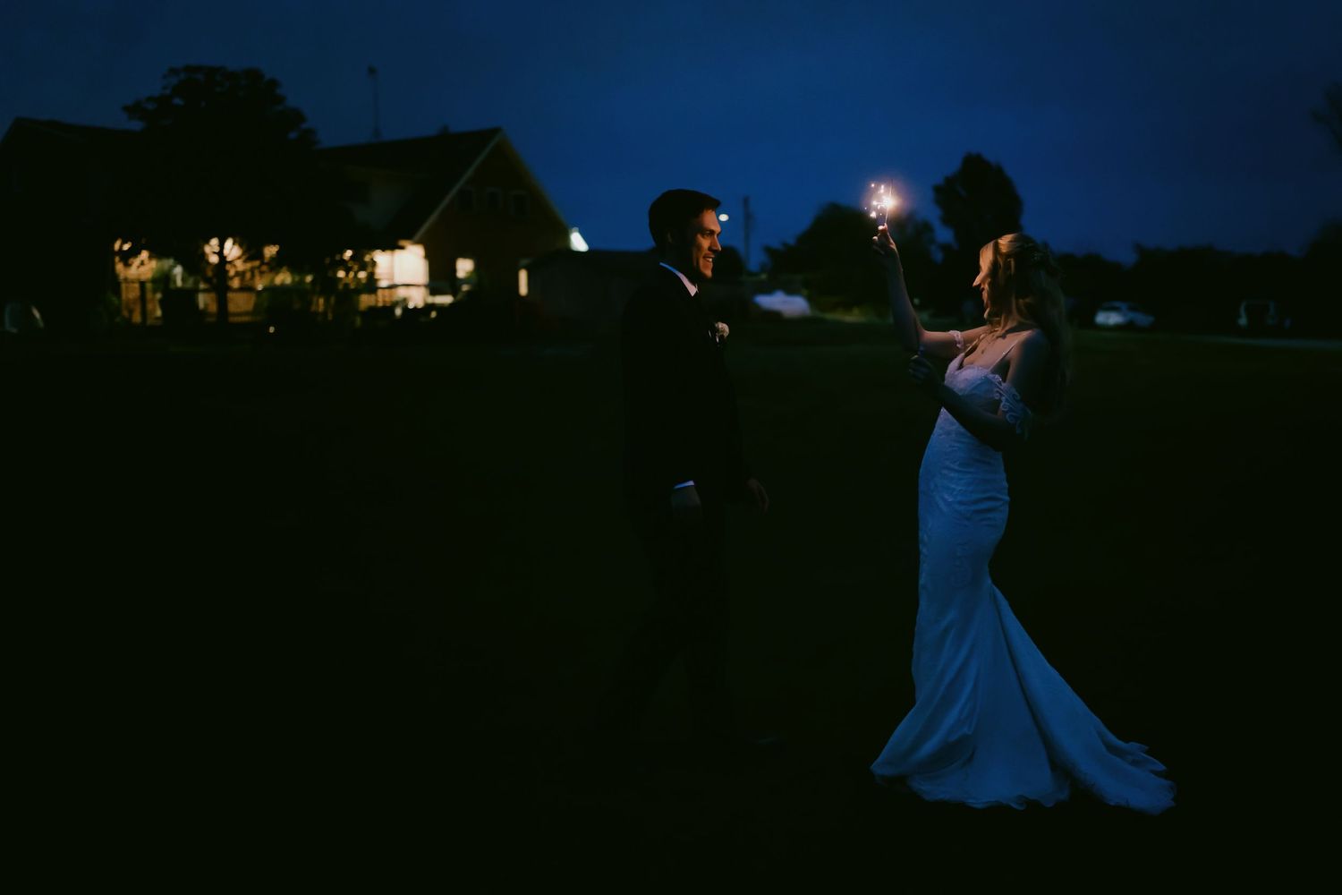 Bride and groom smiling while holding sparklers during night portraits