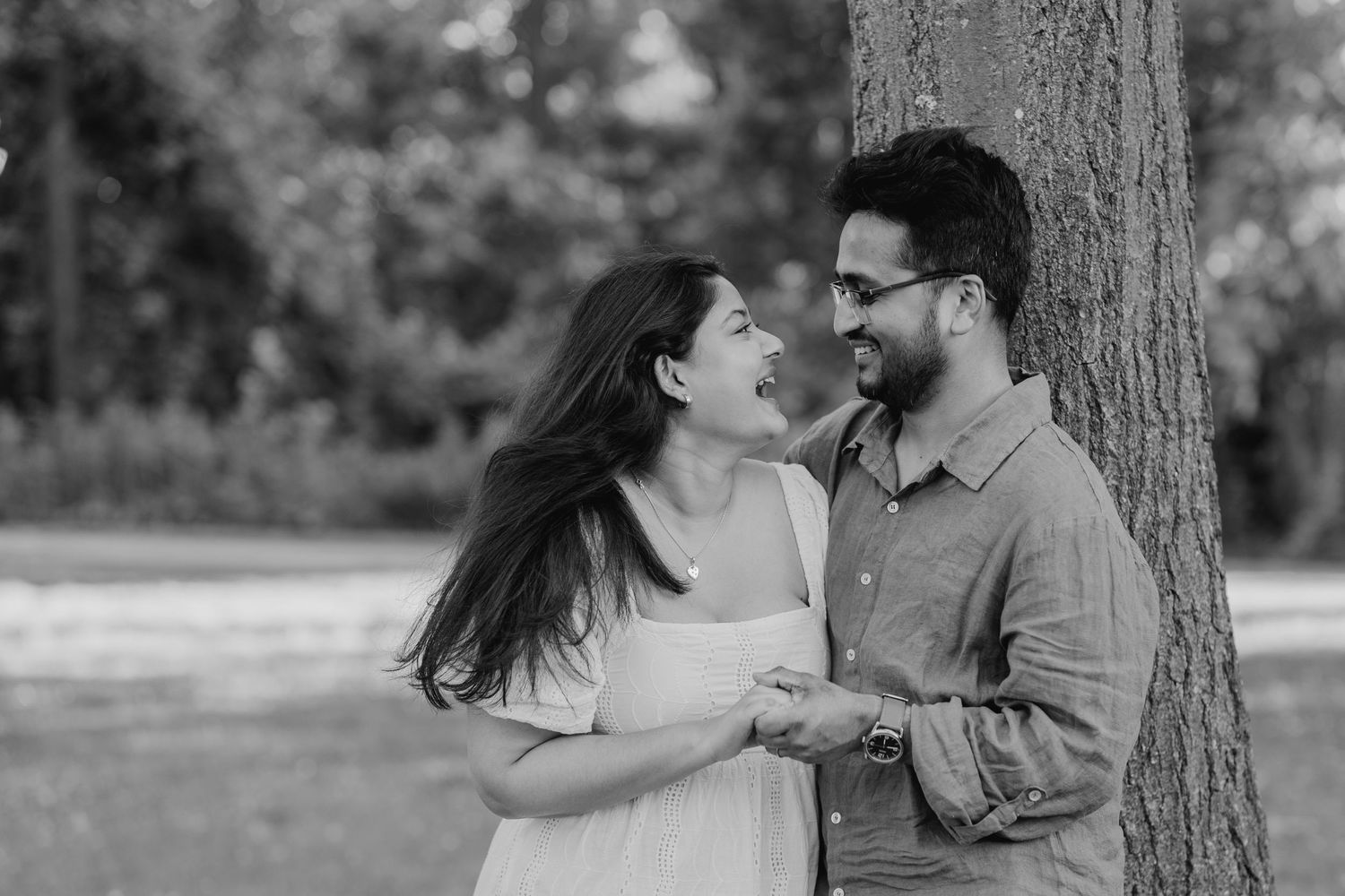 Black and white candid photo of couple laughing beside a tree in the park