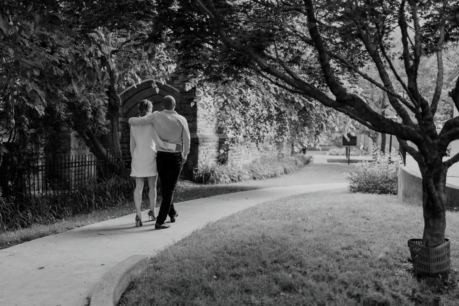 Black and white photo of couple walking along curved path beneath trees