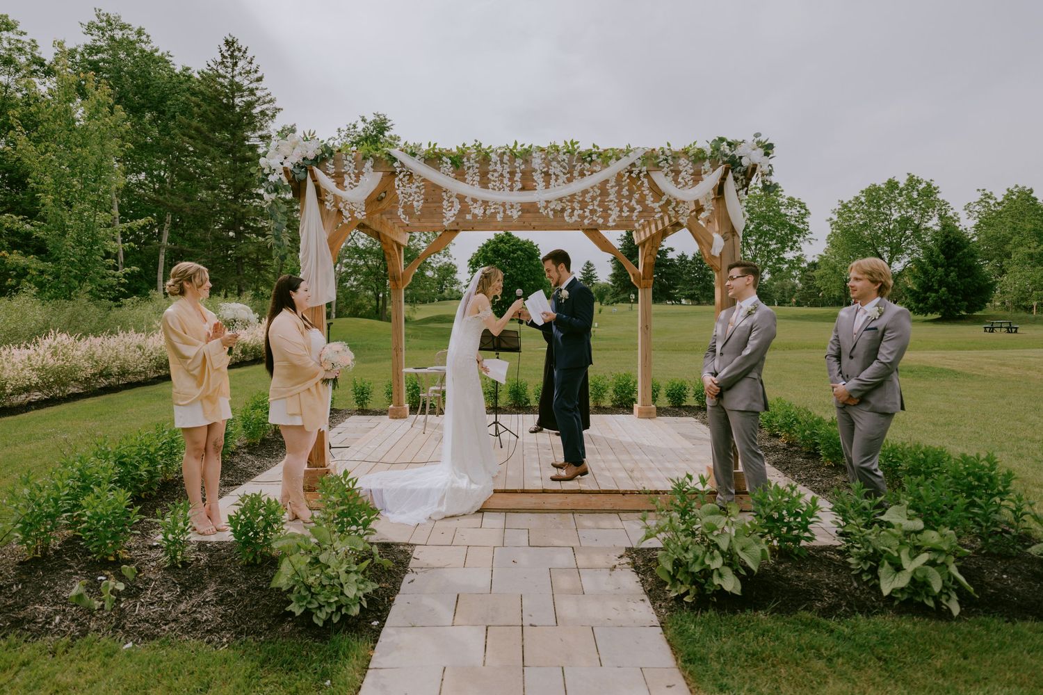 Full view of outdoor wedding ceremony with bridal party and floral arch