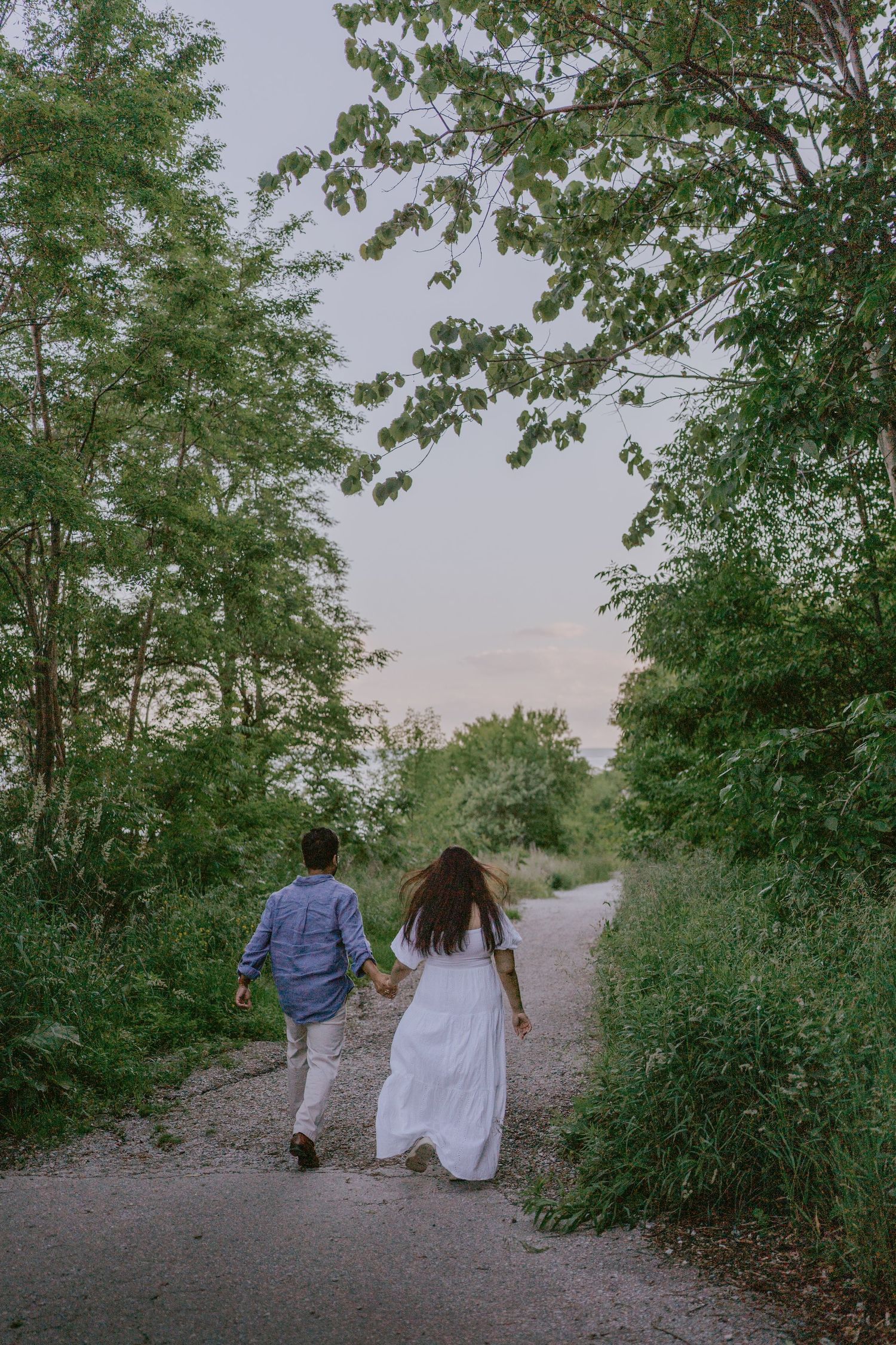 Romantic outdoor photo of couple walking hand-in-hand down wooded trail