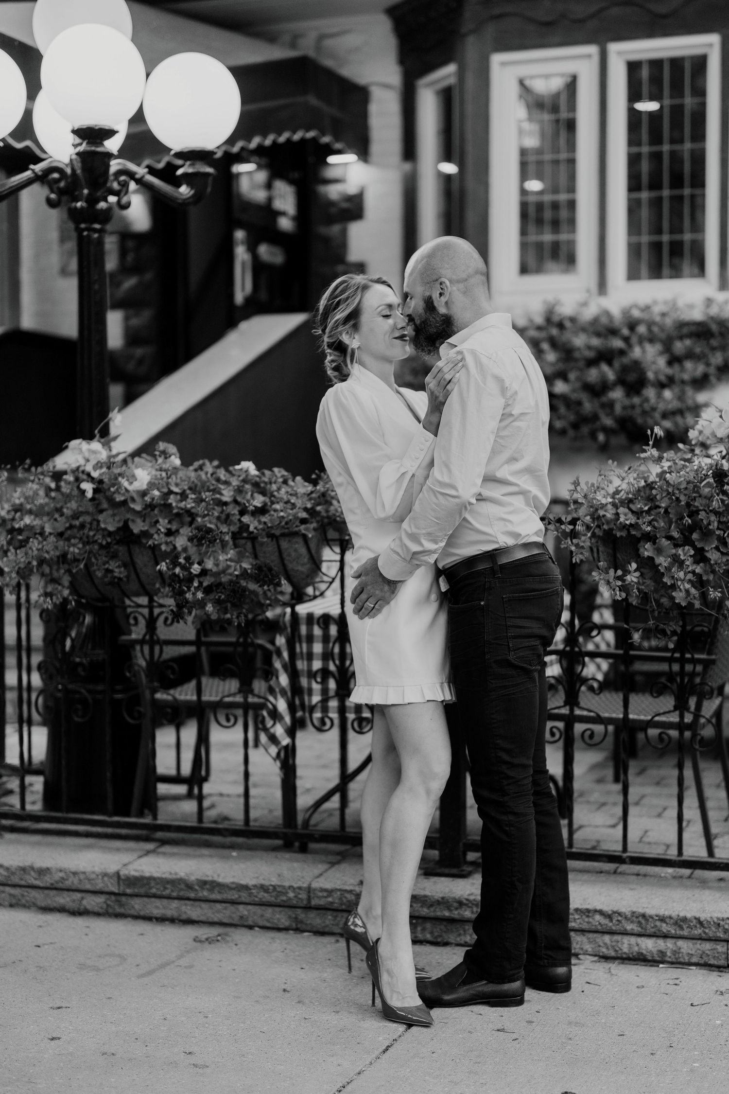Black and white engagement photo of couple near patio lights and city cafe