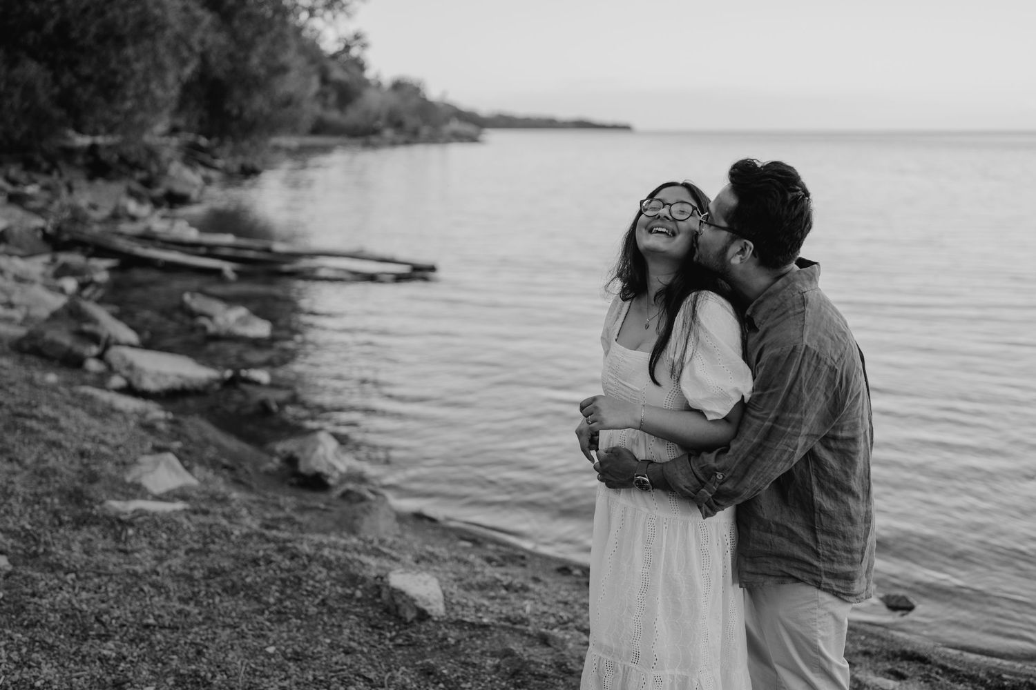 Black and white engagement photo of couple hugging by the shoreline