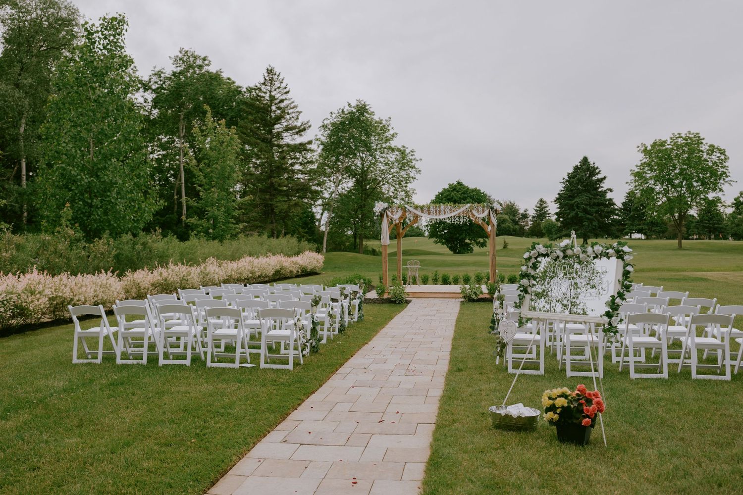 Wide-angle photo of wedding ceremony setup with white chairs and floral arch