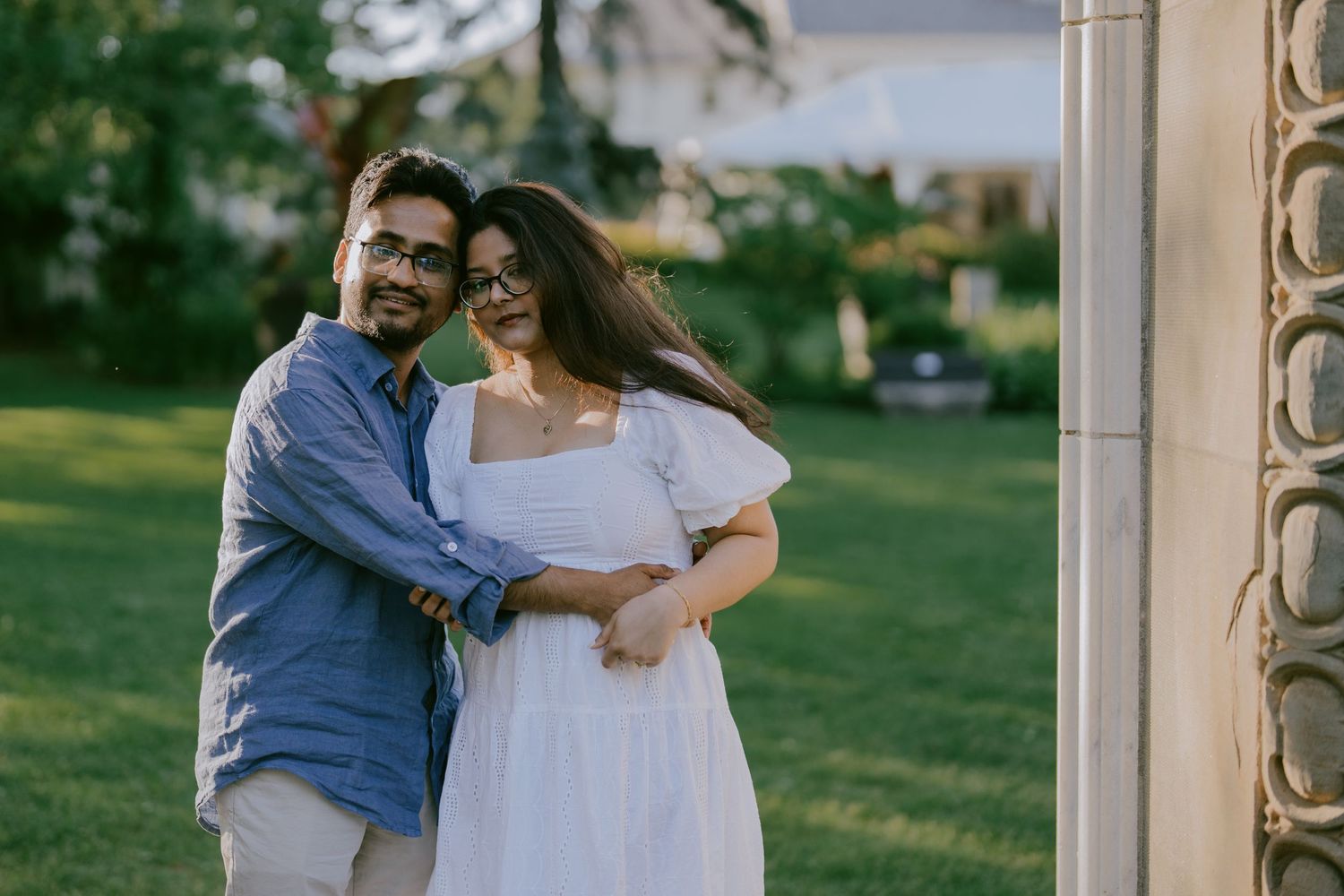 Engagement photo of couple laughing and hugging near stone garden columns
