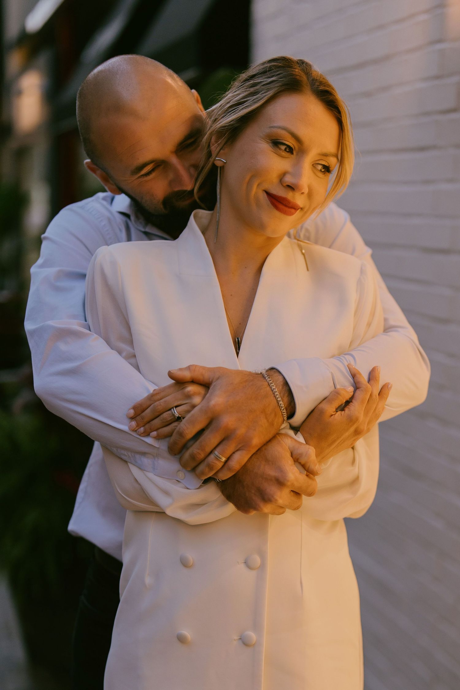 Romantic golden hour photo of couple embracing near soft-lit white wall