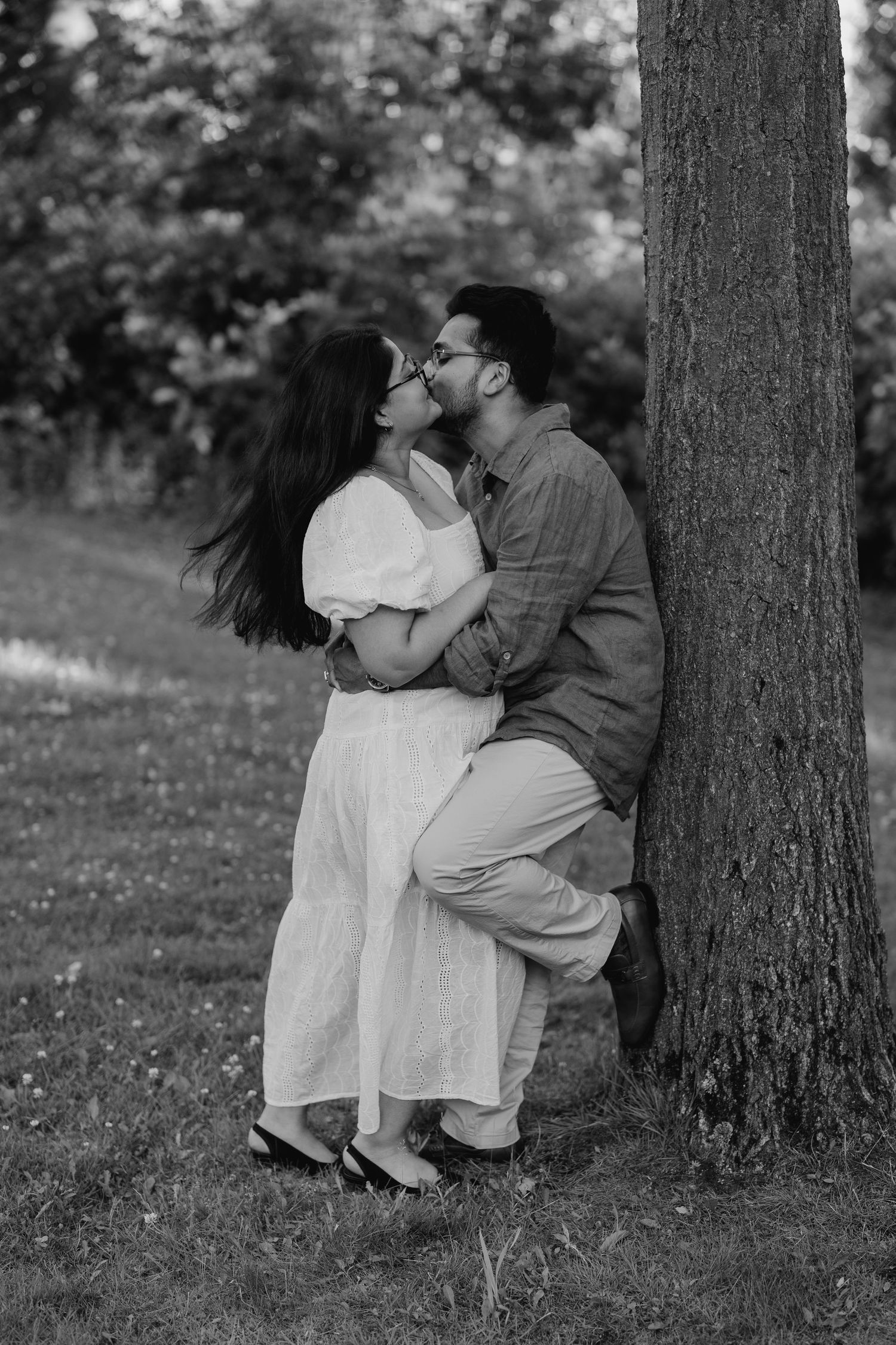 Romantic black and white engagement photo of man lifting woman by a tree