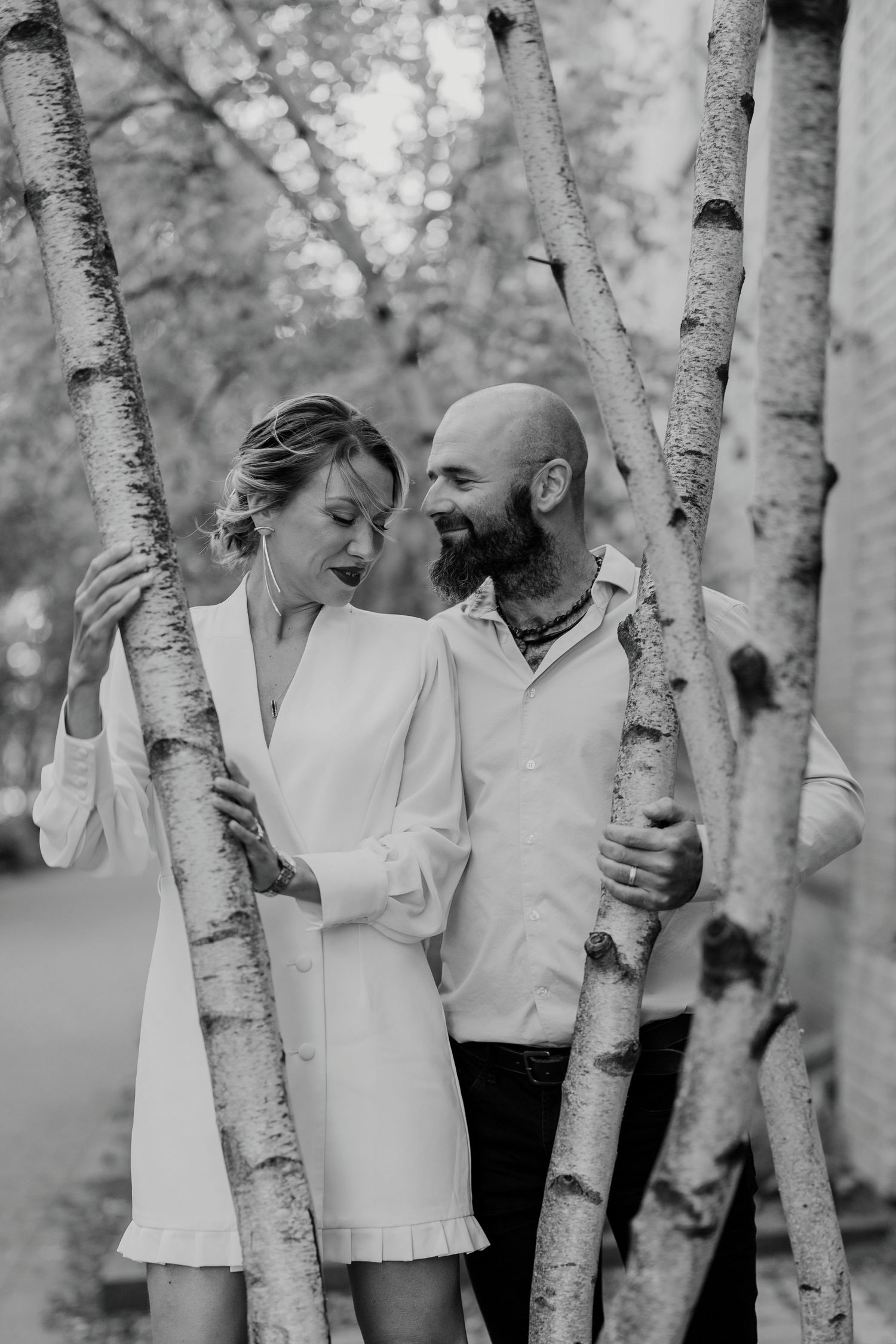 Black and white engagement photo of couple standing closely among birch trees