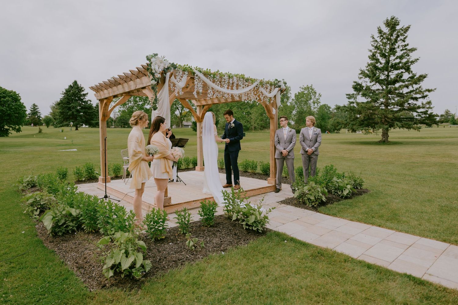 Distant shot of wedding ceremony under wooden arch with guests seated