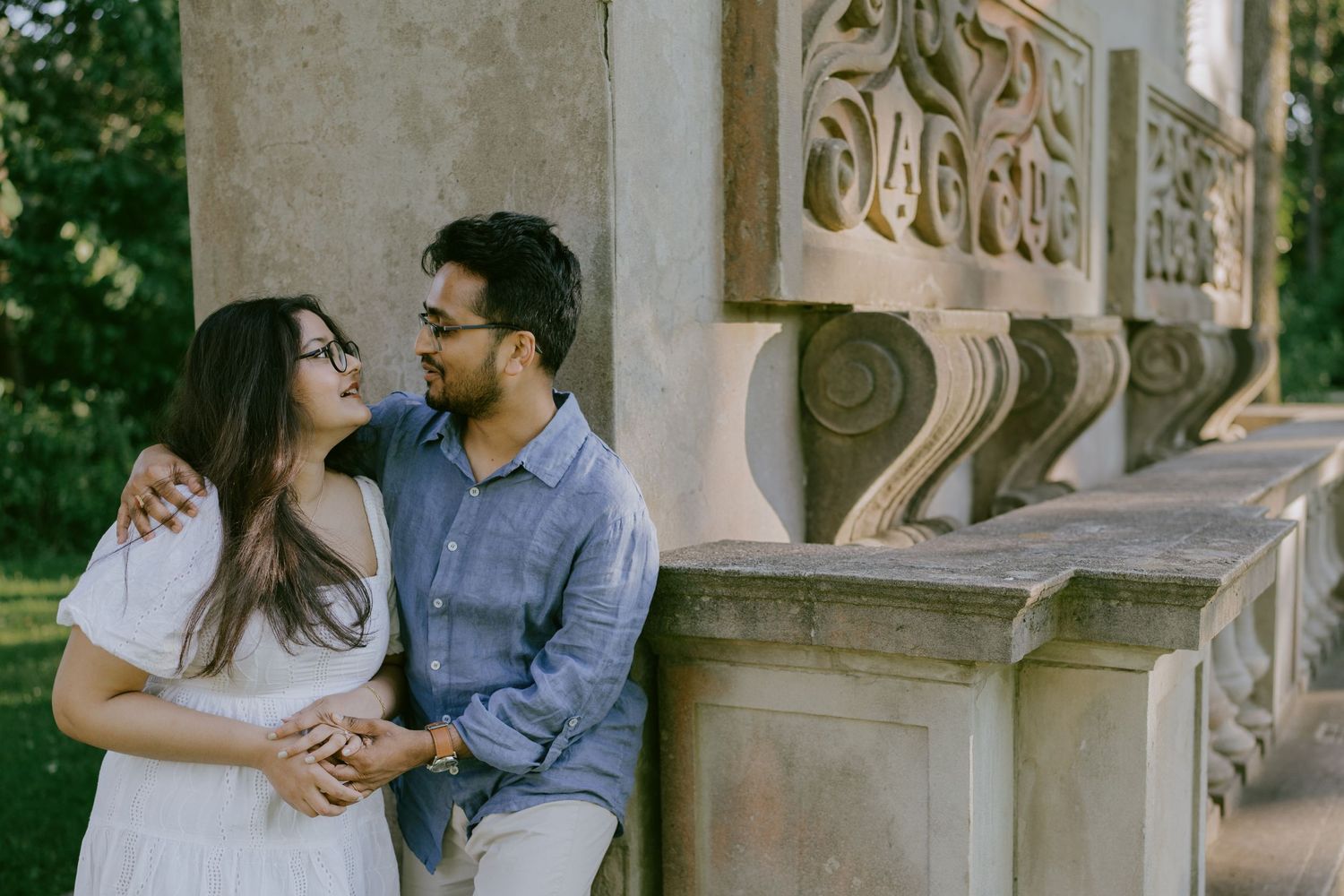 Romantic engagement photo of couple sitting by carved stone architecture, smiling