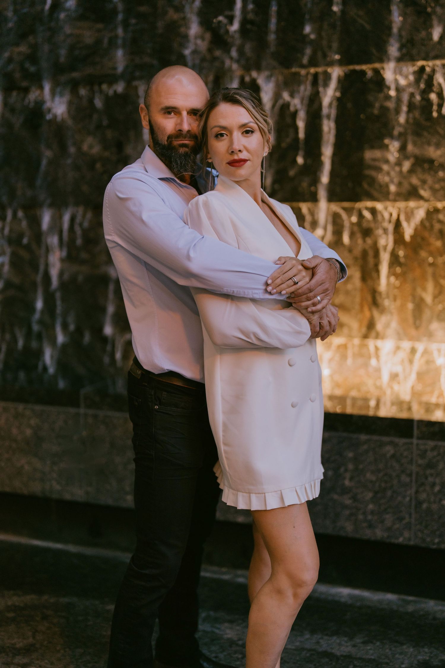 Editorial-style couple portrait with close embrace, posed in front of stone water wall