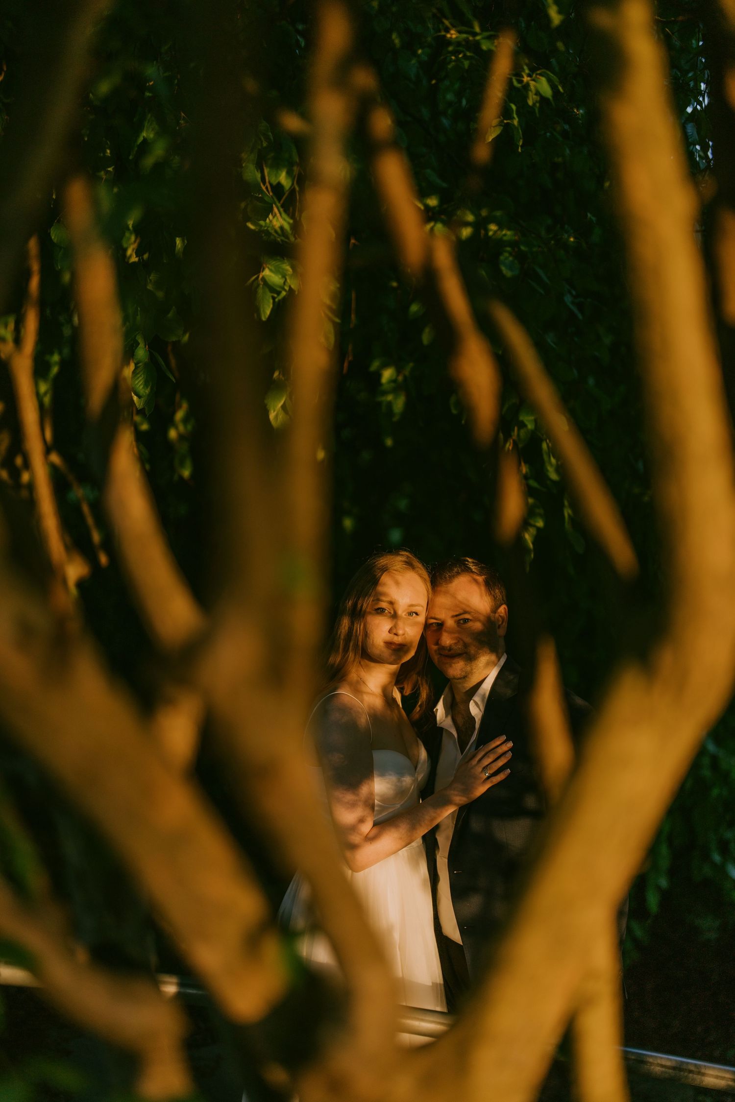 Creative engagement photo of couple peeking through branches in golden light in Toronto