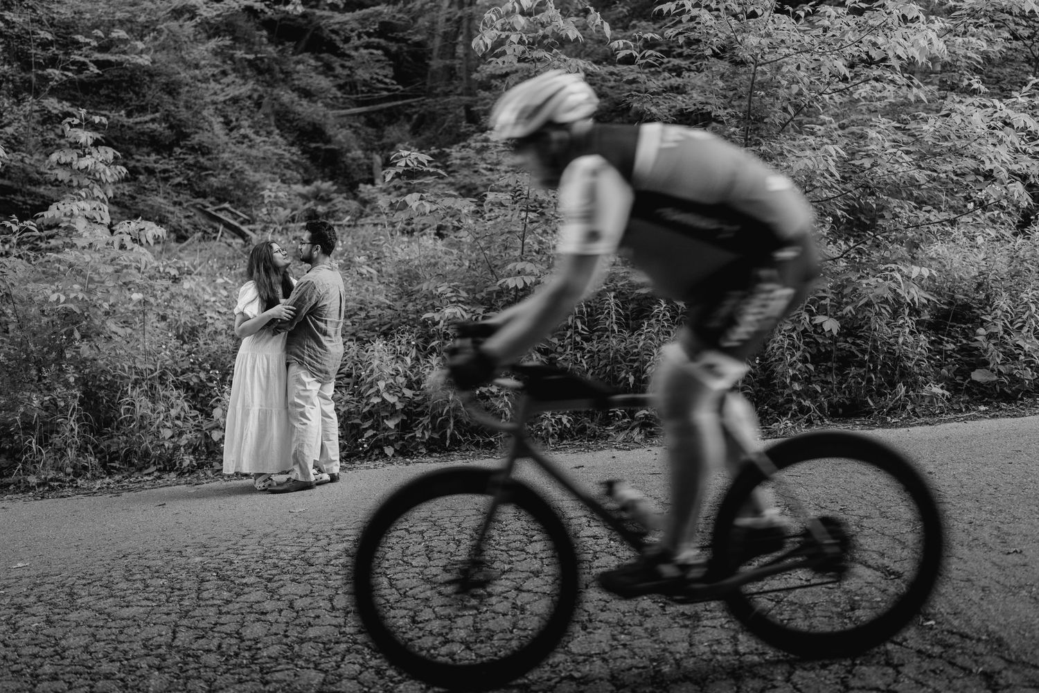 Black and white candid moment of cyclist riding past couple in forest path