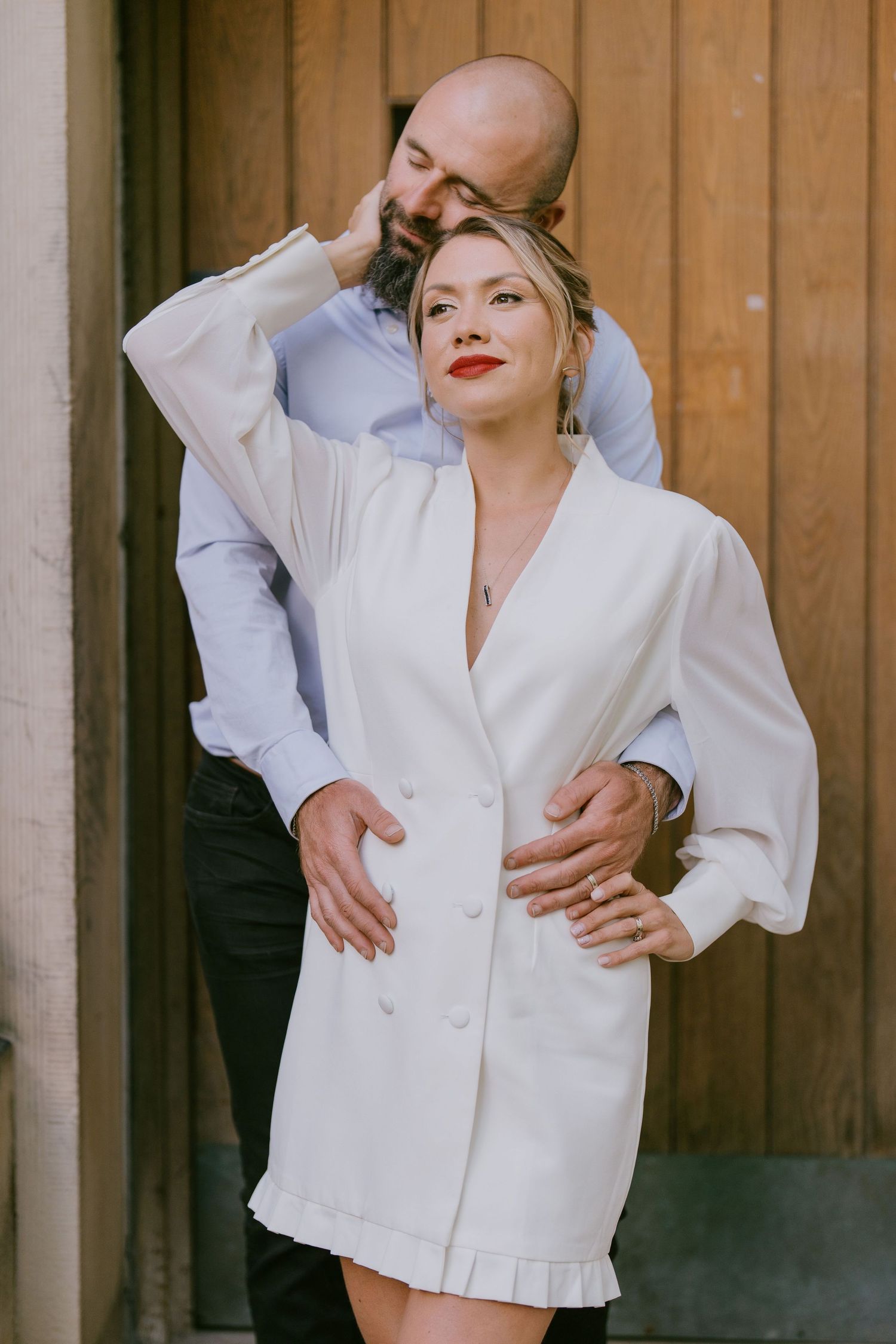 Chic editorial-style couple’s portrait with warm embrace in front of modern wood wall