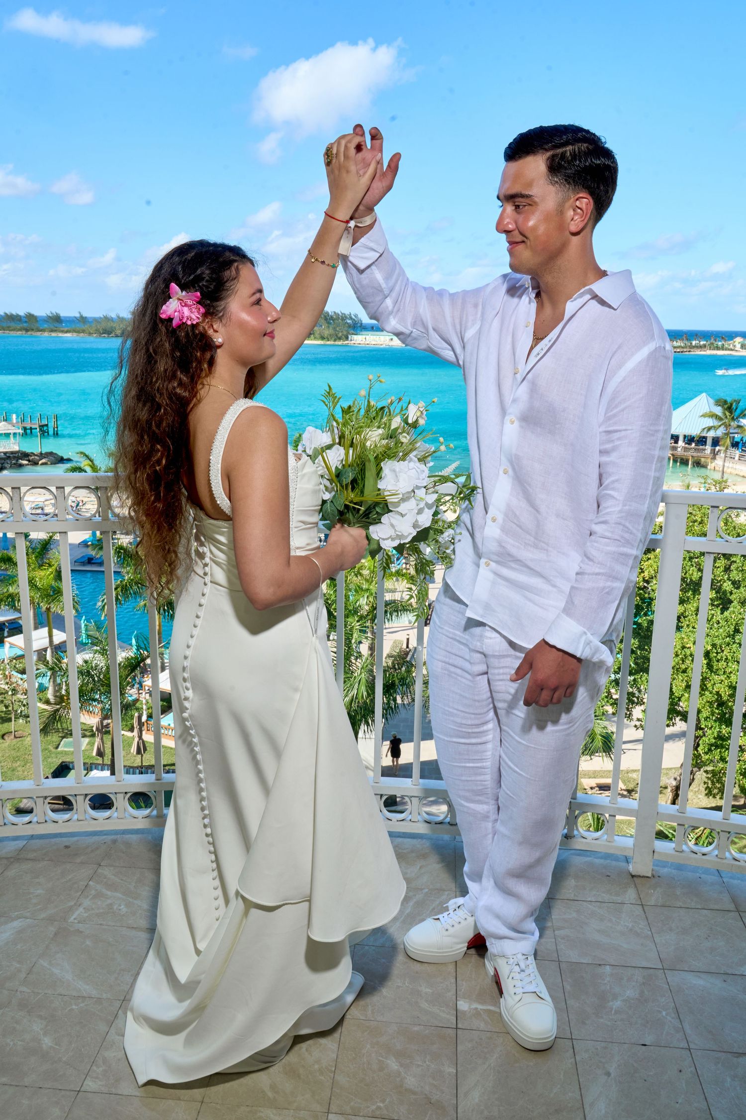 Groom twirls bride holding bouquet on a balcony overlooking beautiful turquoise Caribbean waters.