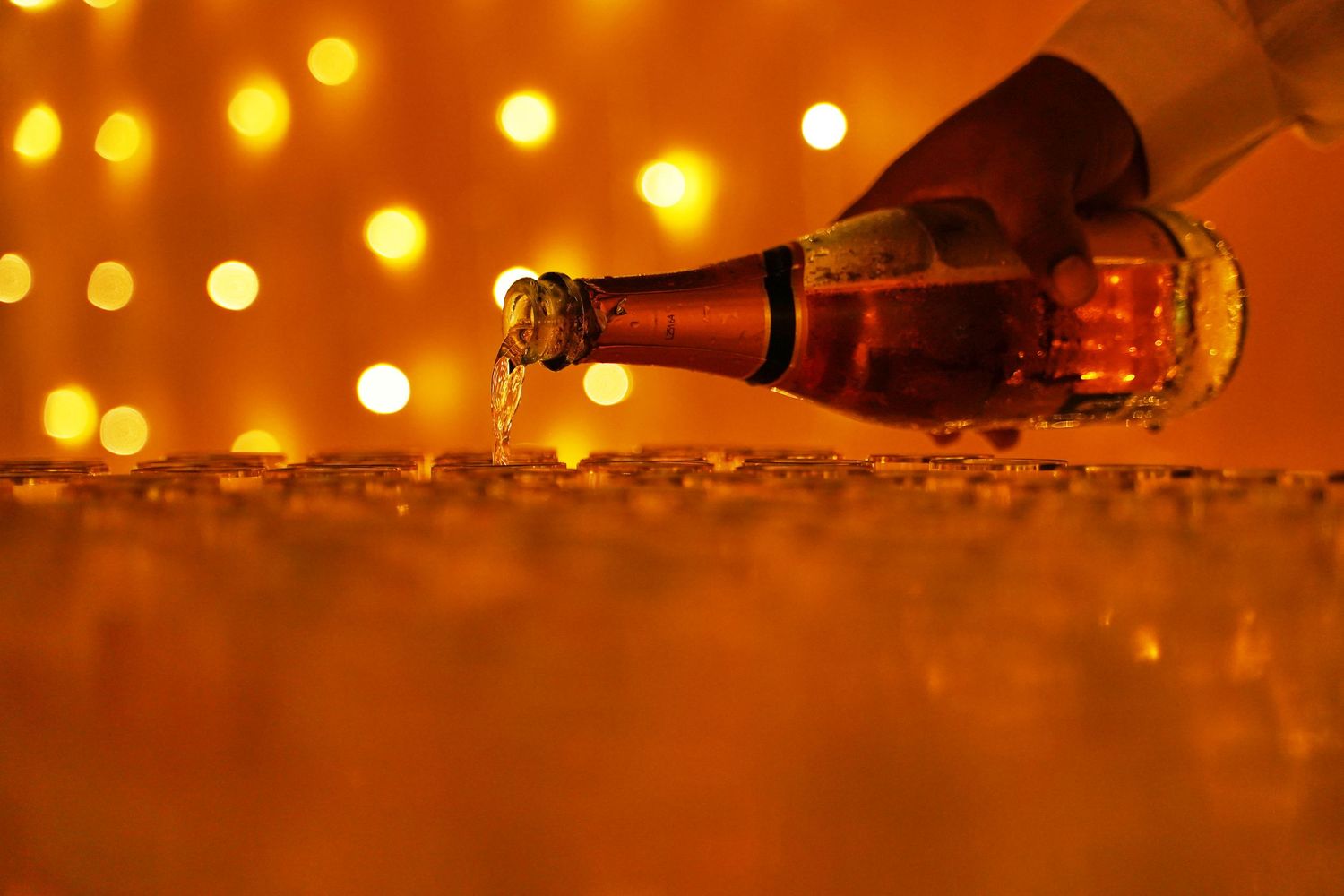 Champagne bottle pouring into glasses with warm golden bokeh lights in the background at a celebration.