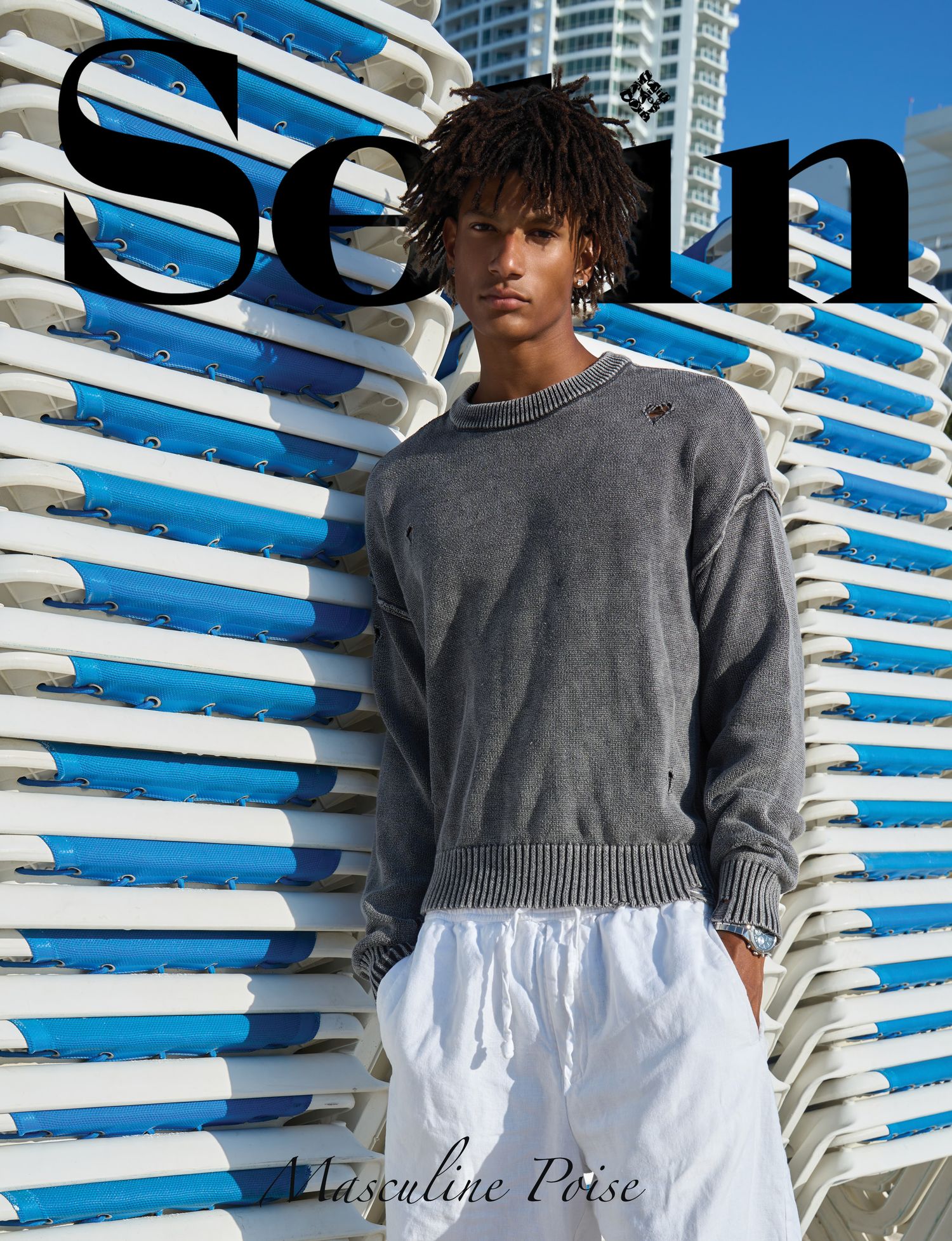 Young male model in gray sweatshirt and white shorts poses against blue and white stacked chairs for Sein magazine cover.